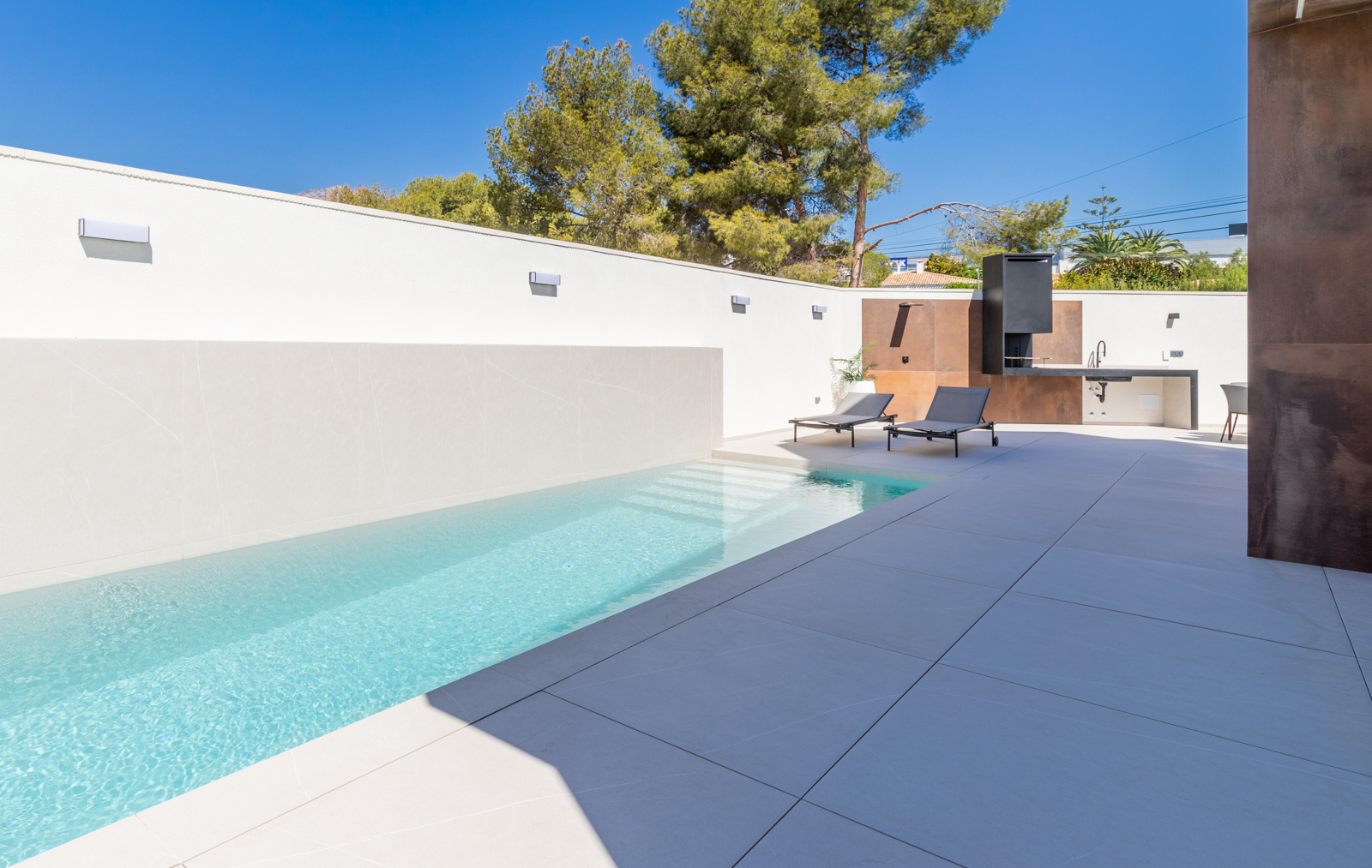 Moderner Pool mit weiß gefliester Wand und Grillbereich mit Betonarbeitsplatte.