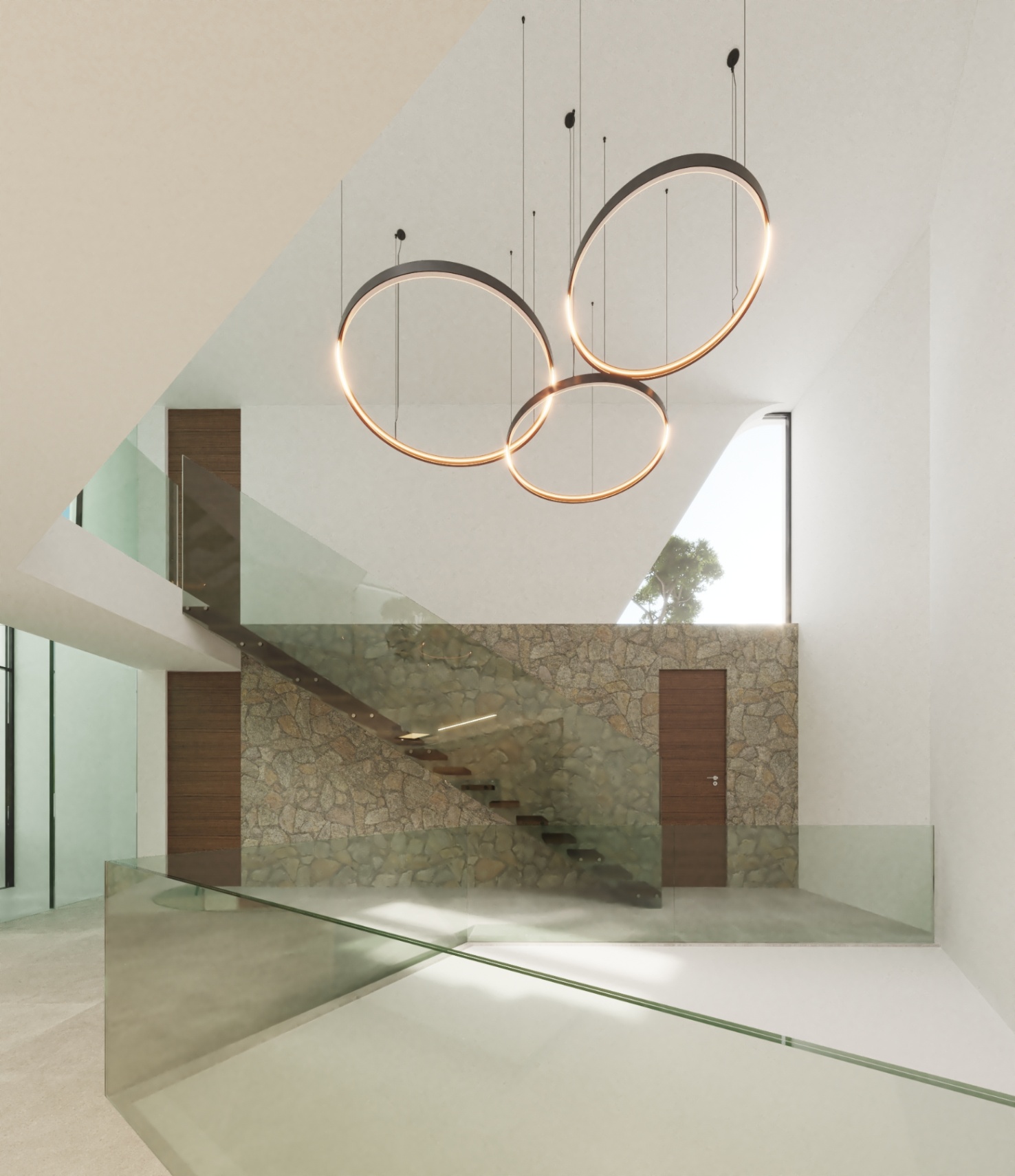 Freischwebende Treppe mit Holzstufen und Glasgeländer vor einer Natursteinwand, beleuchtet durch moderne Ringpendelleuchten in einem offenen, hellen Atrium.