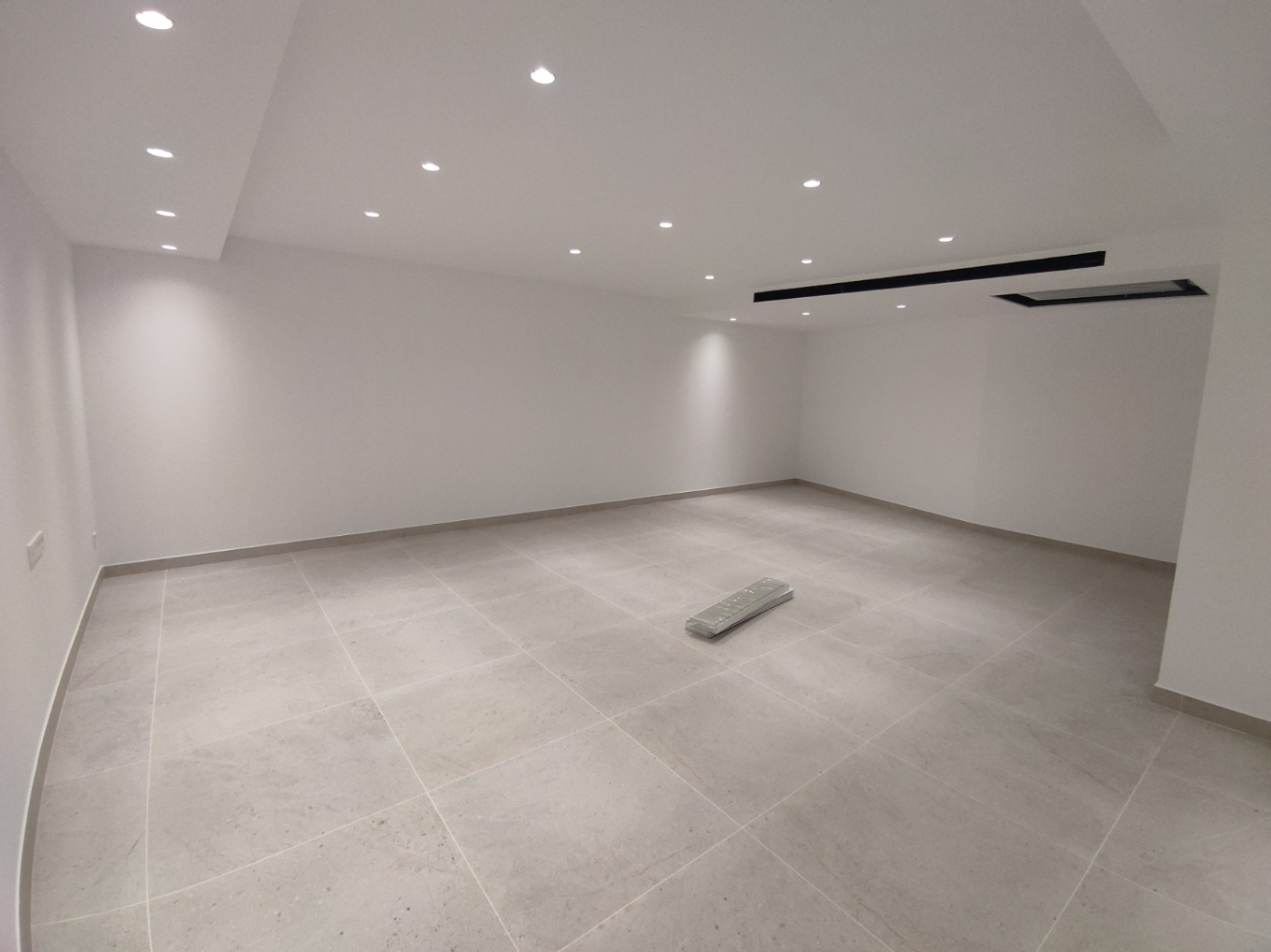 Großer, offener Raum mit großformatigen Feinsteinzeugfliesen, weißen Wänden und einer modernen Deckenbeleuchtung mit LED-Einbaustrahlern.