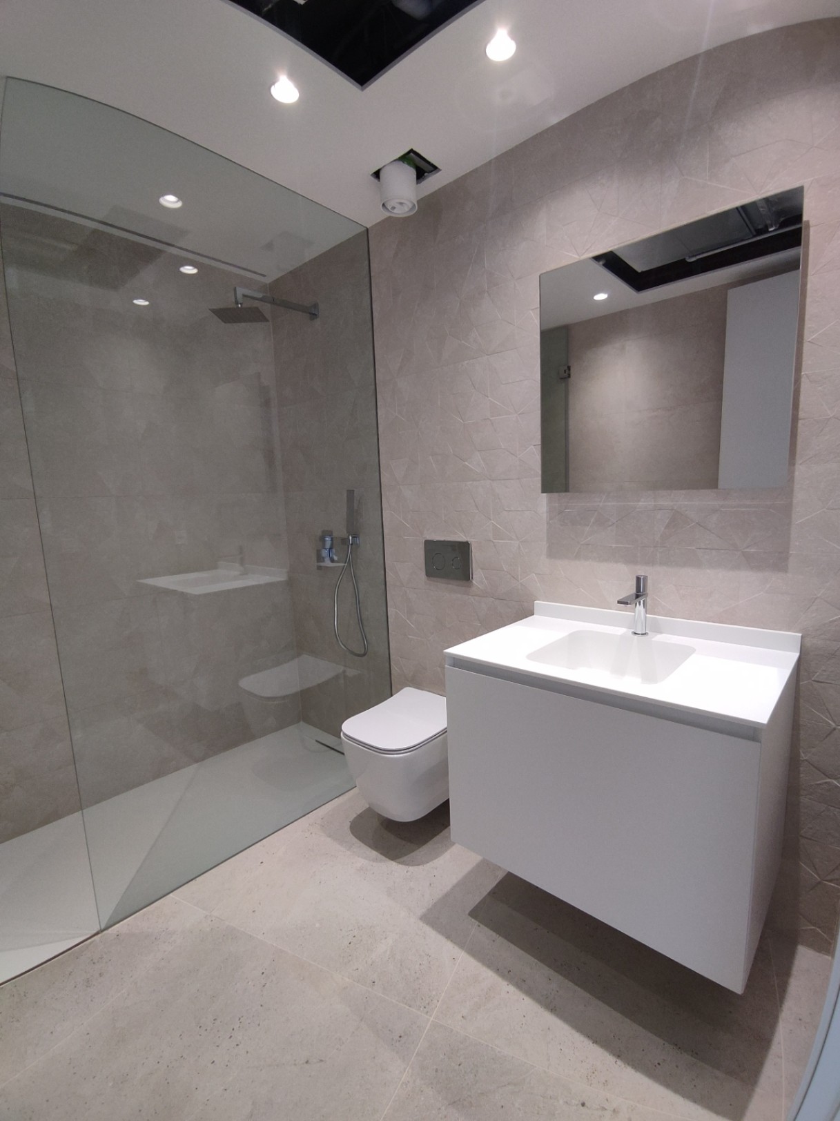 Modernes Badezimmer mit begehbarer Glasdusche, wandhängendem WC und weißem, schwebendem Waschtisch vor geometrisch strukturierten Wandfliesen.