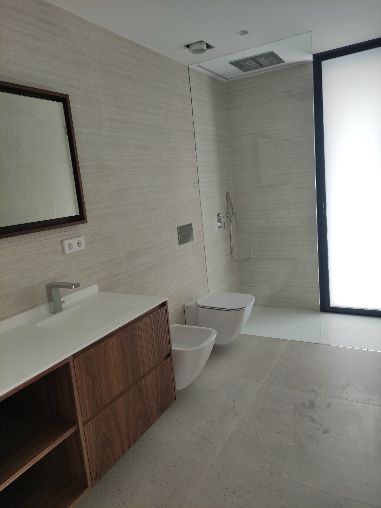 Modernes Badezimmer mit Holzwaschtisch, wandhängendem WC und Bidet sowie einer begehbaren Dusche mit Deckeneinbau-Regenbrause und Glastrennwand.