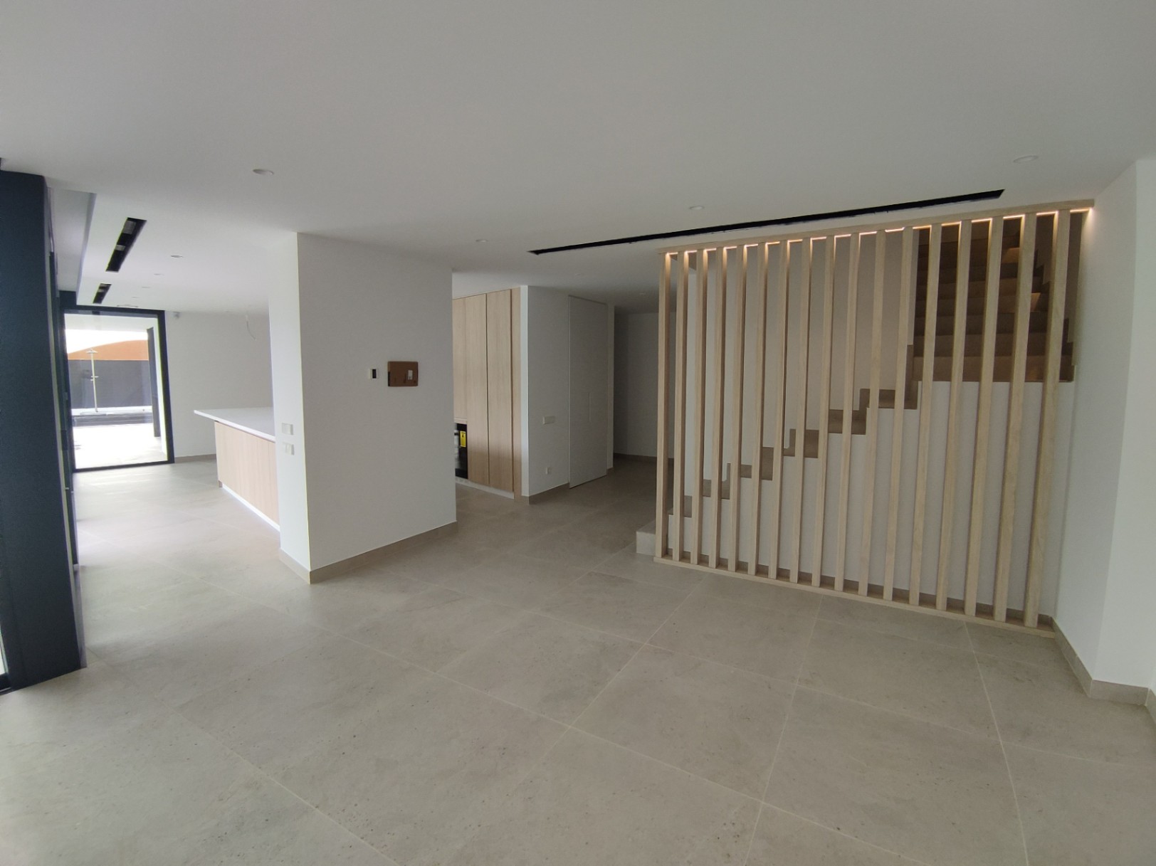 Offener Wohnbereich mit großformatigen Fliesen und einer modernen Treppe, die durch vertikale Holzlamellen und integrierte LED-Akzente besticht.