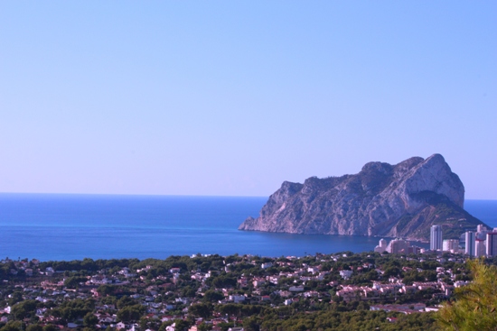 Panoramablick auf den Peñón de Ifach und das Mittelmeer, mit der Küstenlinie von Calpe und üppigem Grün unter strahlend blauem Himmel.
