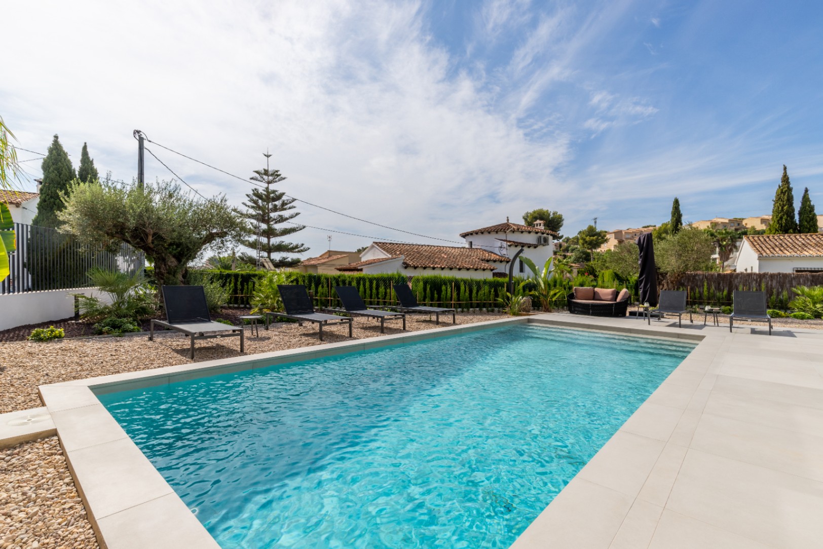 Ansicht des privaten Pools mit hellem Steinrand, umgeben von schwarzen Sonnenliegen und mediterranen Gärten.