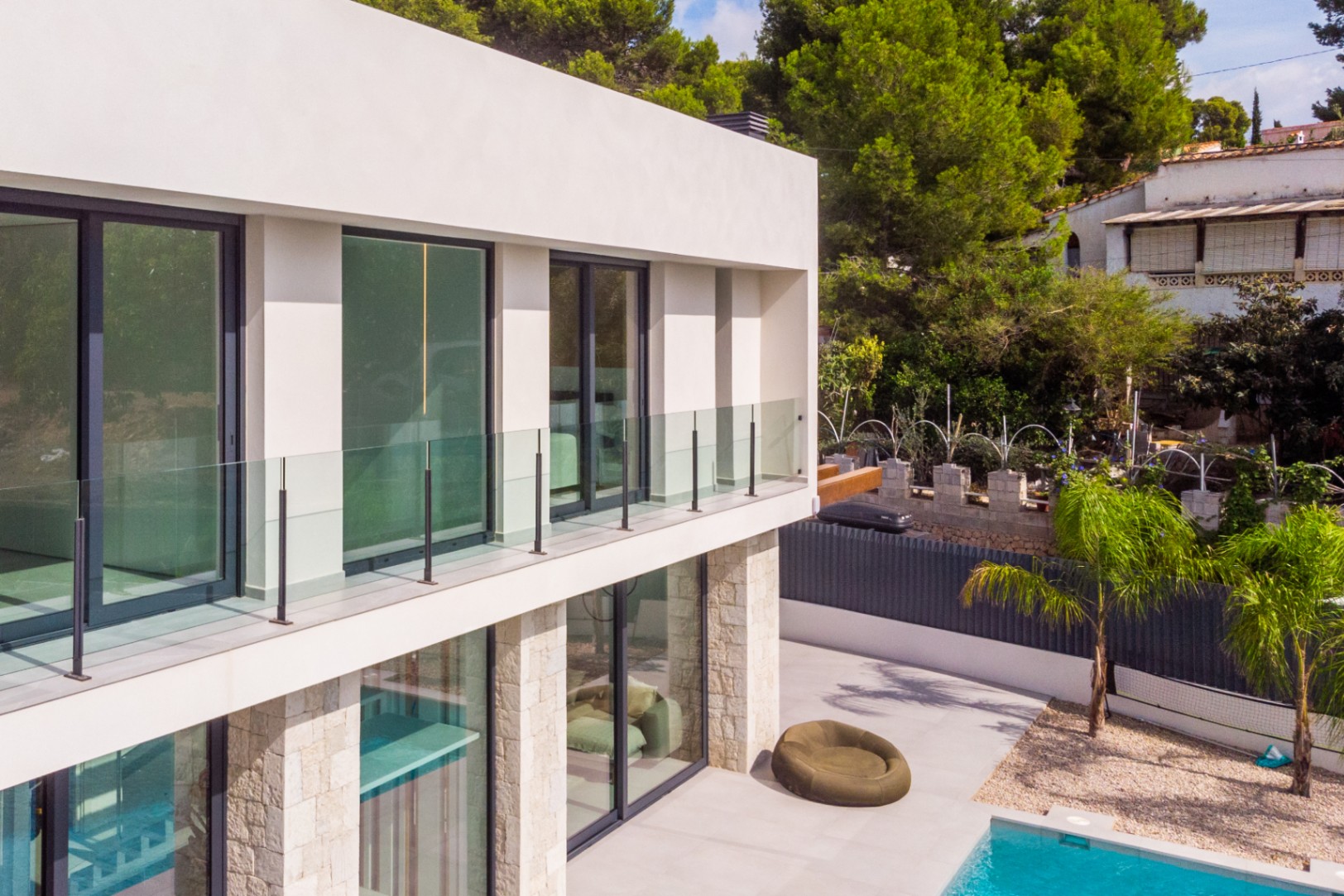 Außenansicht der Villa mit Glasbalkonen, Steinverkleidung und türkisfarbenem Pool.