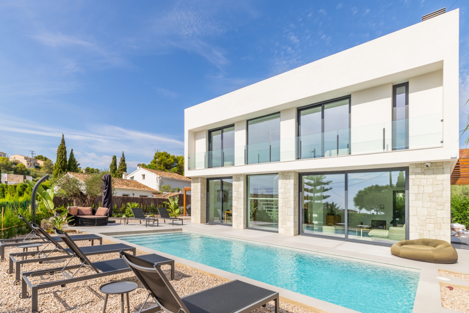 Außenansicht der Villa mit länglichem Pool, umgeben von Kies und schwarzen Sonnenliegen.
