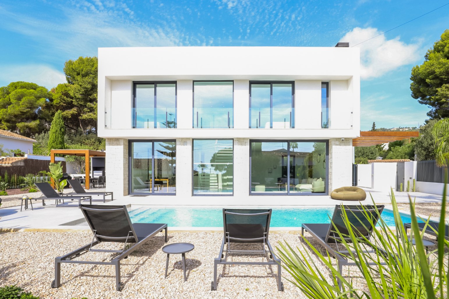 Außenansicht der Villa mit Pool, Liegestühlen und Steinfassade mit großen Fenstern.