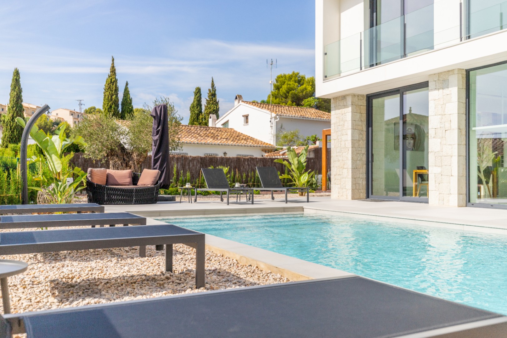 Blick auf den Pool mit grauen Liegestühlen und Lounge-Bereich im Freien mit terrakottafarbenen Kissen.