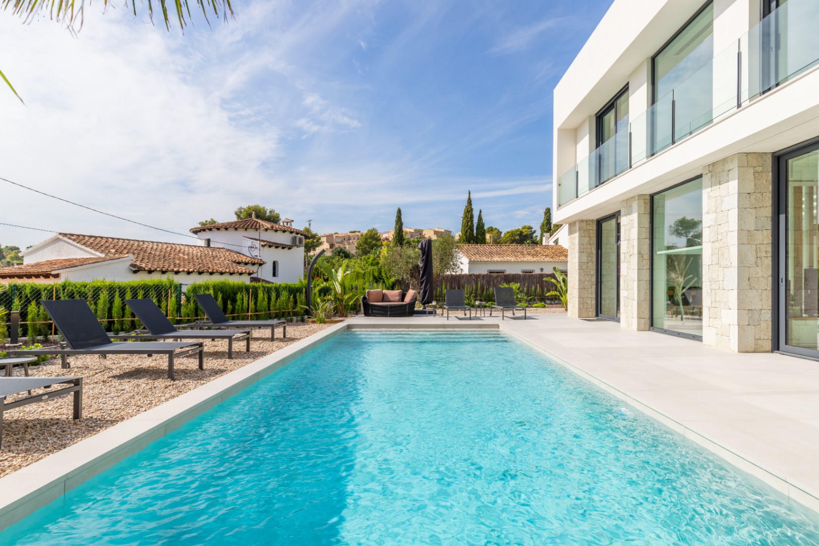 Blick auf den türkisfarbenen Pool, umgeben von Liegestühlen und der modernen Steinfassade der Villa.