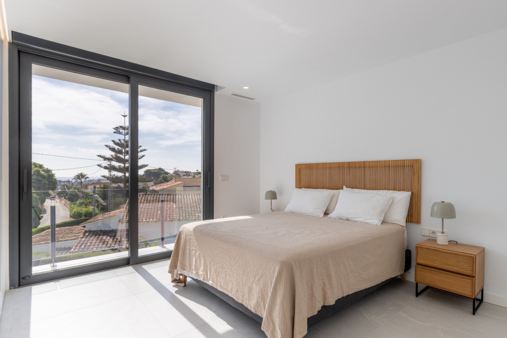 Helles Schlafzimmer mit Doppelbett, Holzkopfteil und Blick nach draußen.