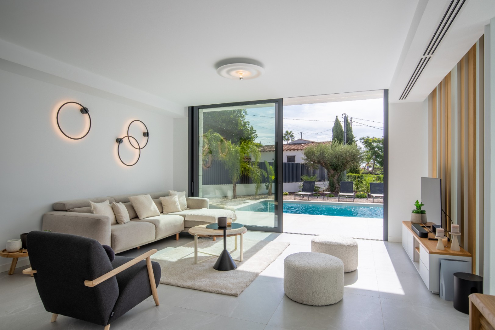 Helles Wohnzimmer mit direktem Poolzugang, kreisförmigen Wandleuchten und moderner Möblierung.