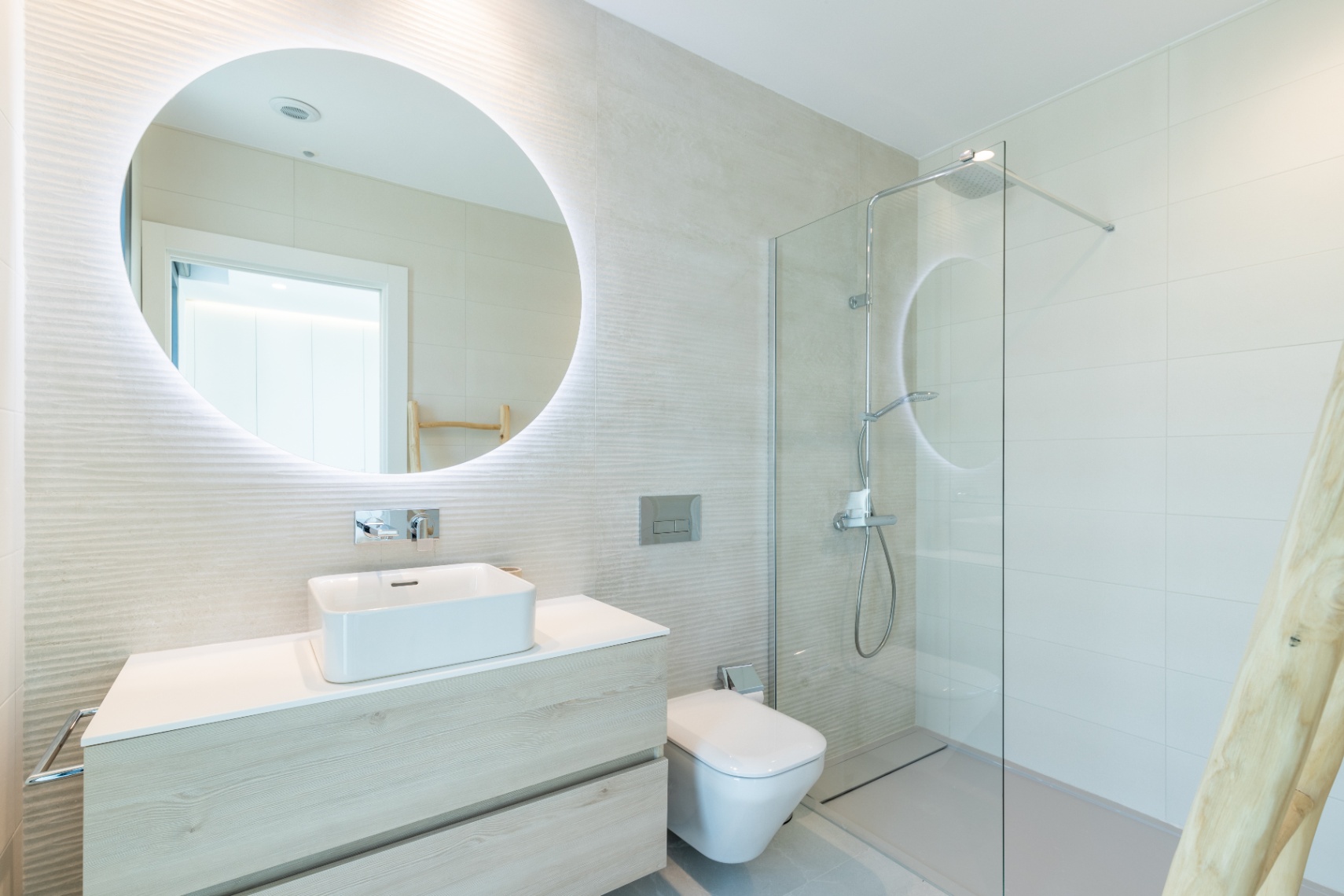 Modernes Badezimmer mit quadratischem Waschbecken, hinterleuchtetem Spiegel und Glasdusche.