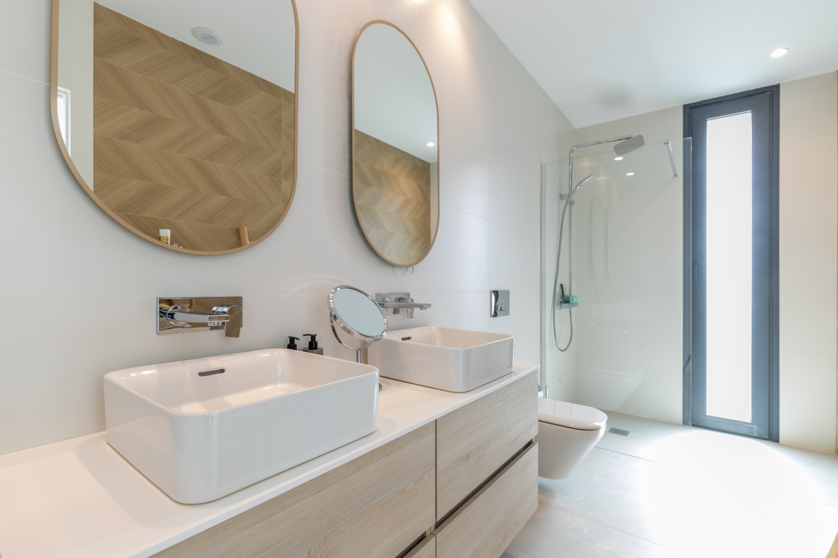 Modernes Badezimmerdetail mit Doppelwaschbecken, ovalen Spiegeln und gläserner Duschkabine.