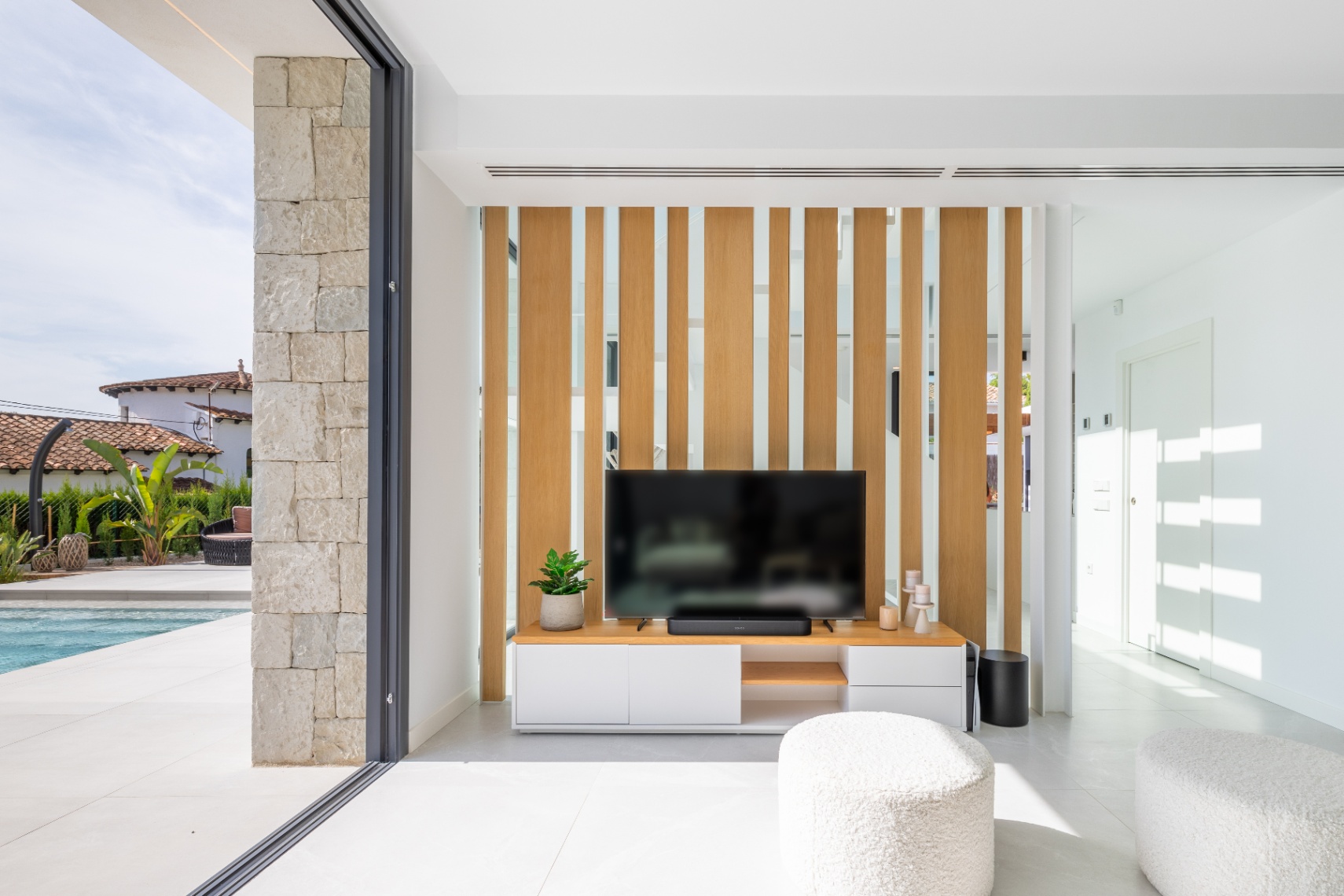Modernes Wohnzimmer mit TV-Möbel und hellem Holzbildschirm. Zugang zur Terrasse mit Pool.
