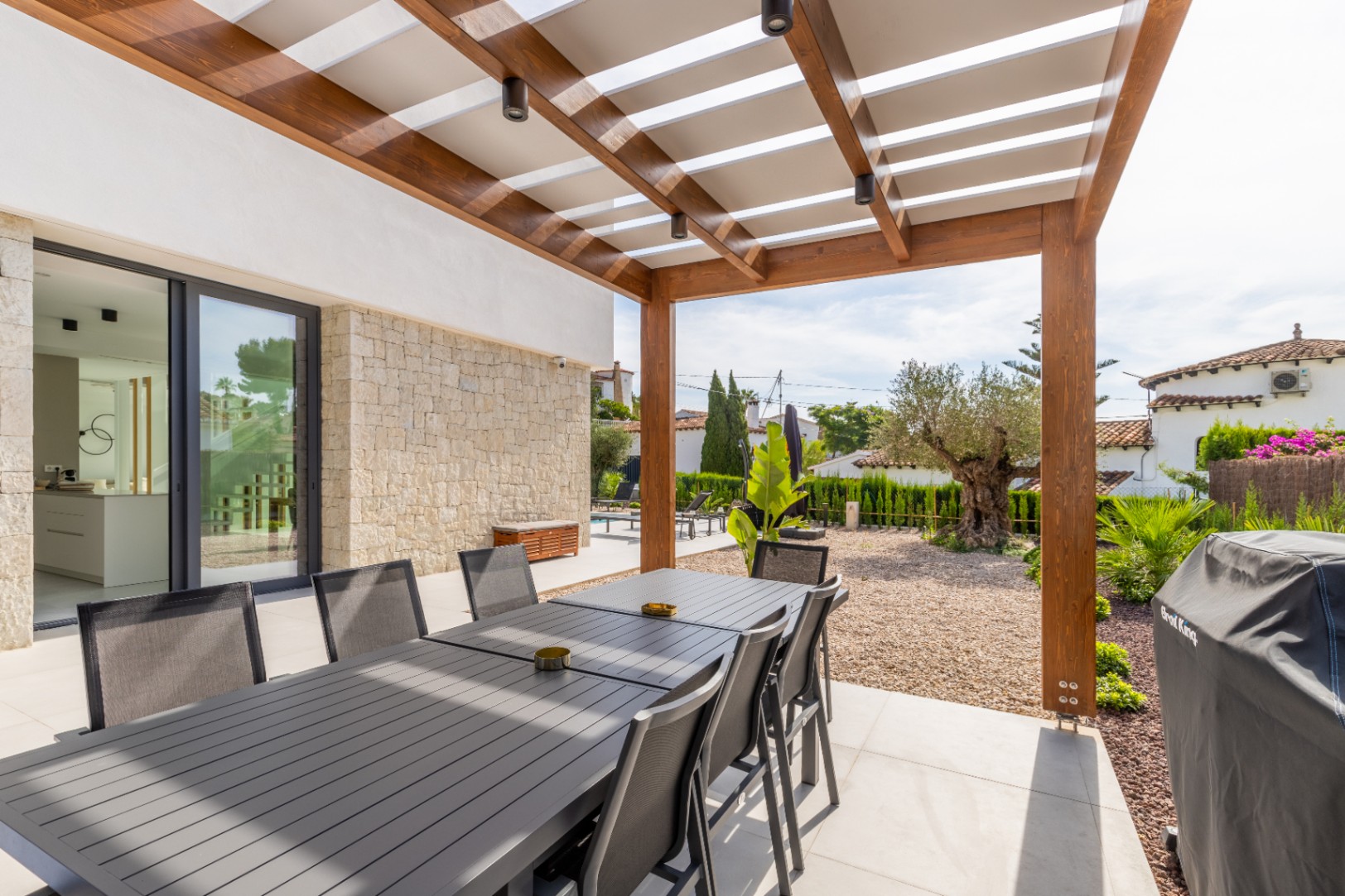 Überdachter Essbereich im Freien mit Holzpergola und Blick auf den mediterranen Garten.