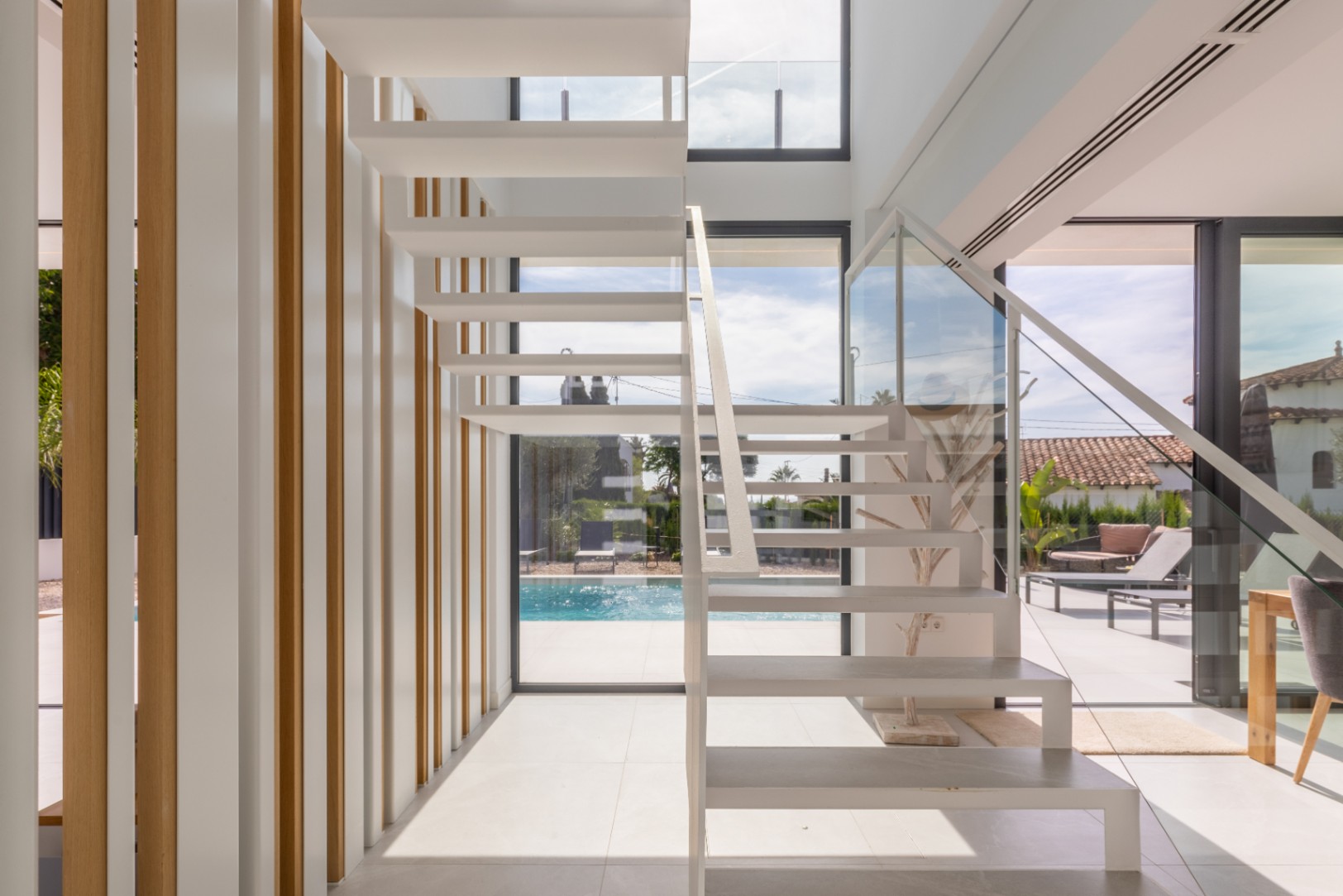 Weiße, freitragende Treppe mit Glasgeländer und vertikalen Lamellen aus hellem Holz.