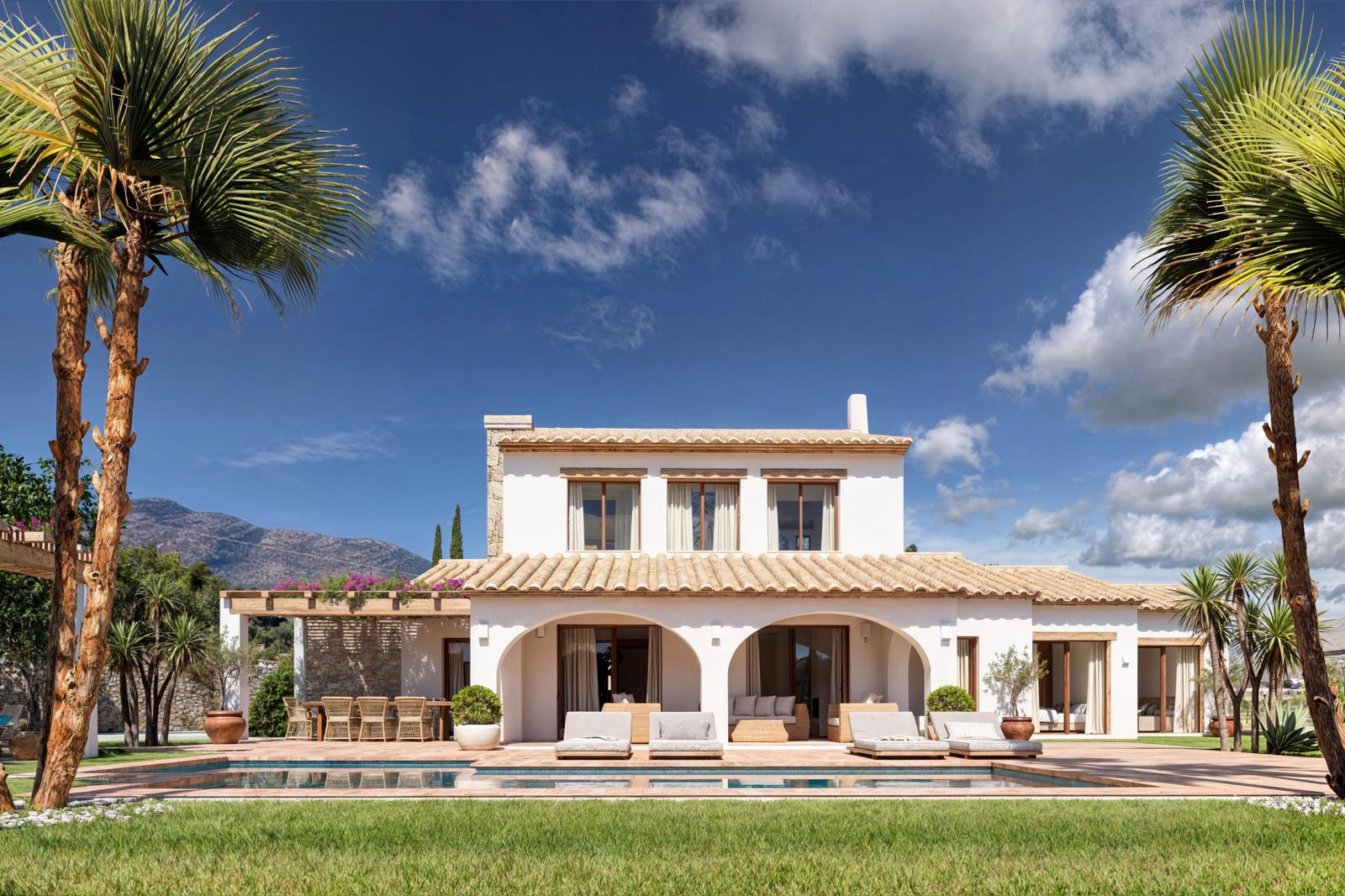 Hauptfassade der Villa mit Rundbogen-Veranda, rechteckigem Pool und Terrakotta-Sonnendeck, eingerahmt von Palmen und Bergblick unter klarem Himmel.