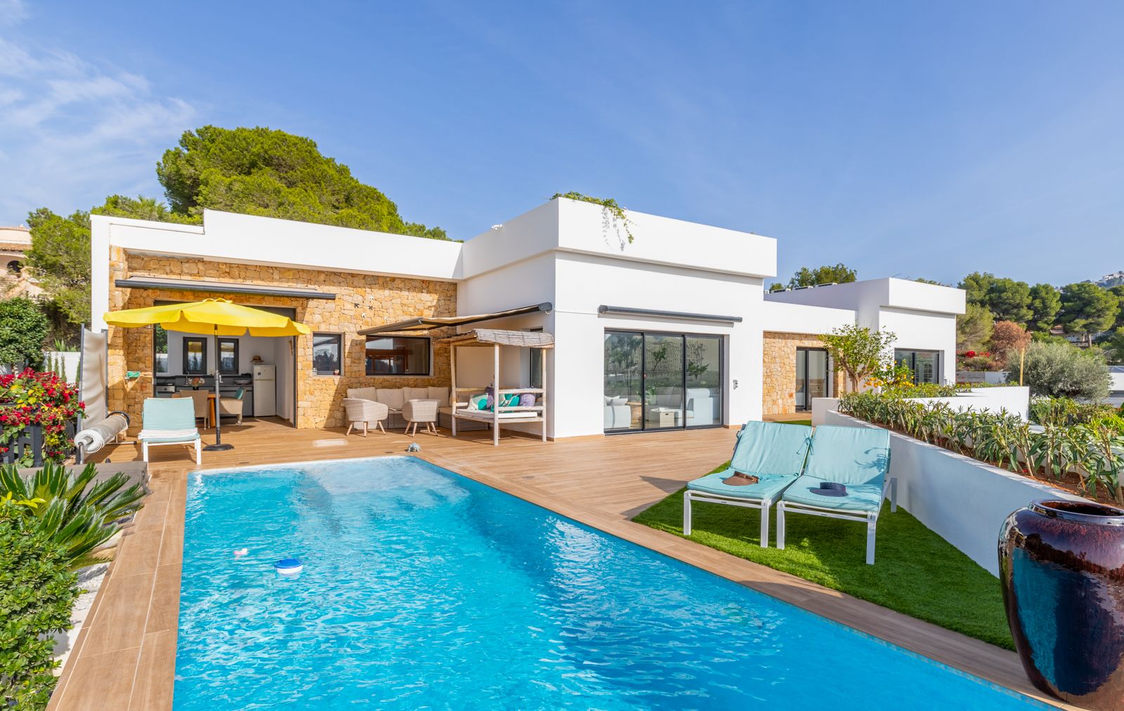 Außenterrasse mit Pool, Feinsteinzeug in Holzoptik und Natursteinwänden. Ausgestattet mit Außenküche, Kunstrasen-Solarium und verschiedenen gemütlichen Loungebereichen.
