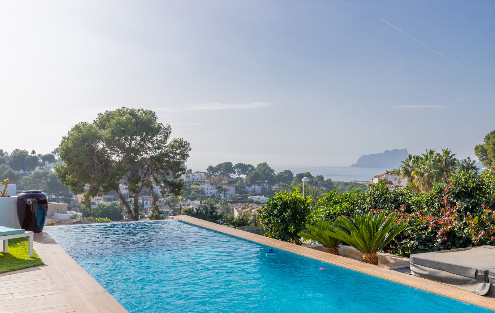 Infinity-Pool mit Panoramablick auf das Mittelmeer und den Peñón de Ifach, ergänzt durch eine helle Steinterrasse und mediterrane Bepflanzung.