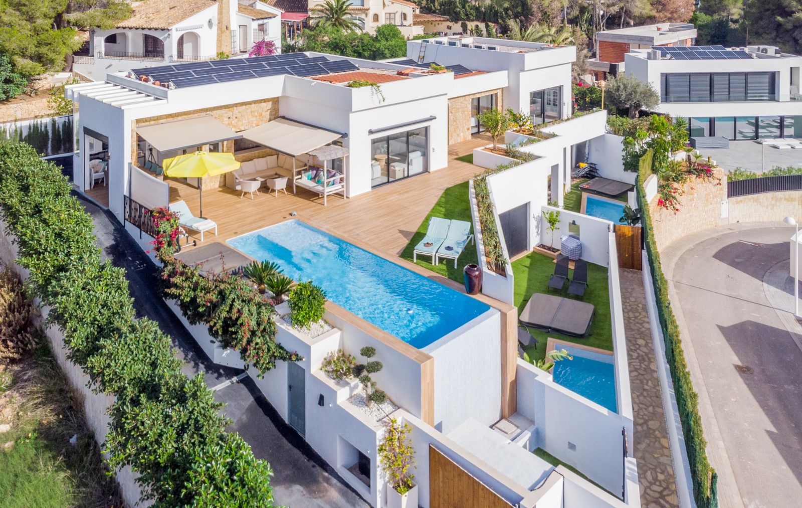 Luftaufnahme der modernen Villa mit Infinity-Pool, weitläufigen Holzterrassen, Solarmodulen auf dem Dach und privaten Außenbereichen für Gästeapartments.