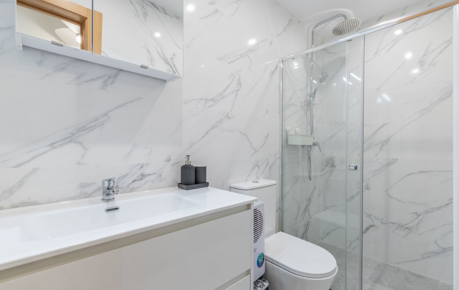 Modernes Badezimmer mit großformatigen Fliesen in Marmoroptik, weißem Waschtisch und einer begehbaren Glasdusche mit Regenduschkopf.