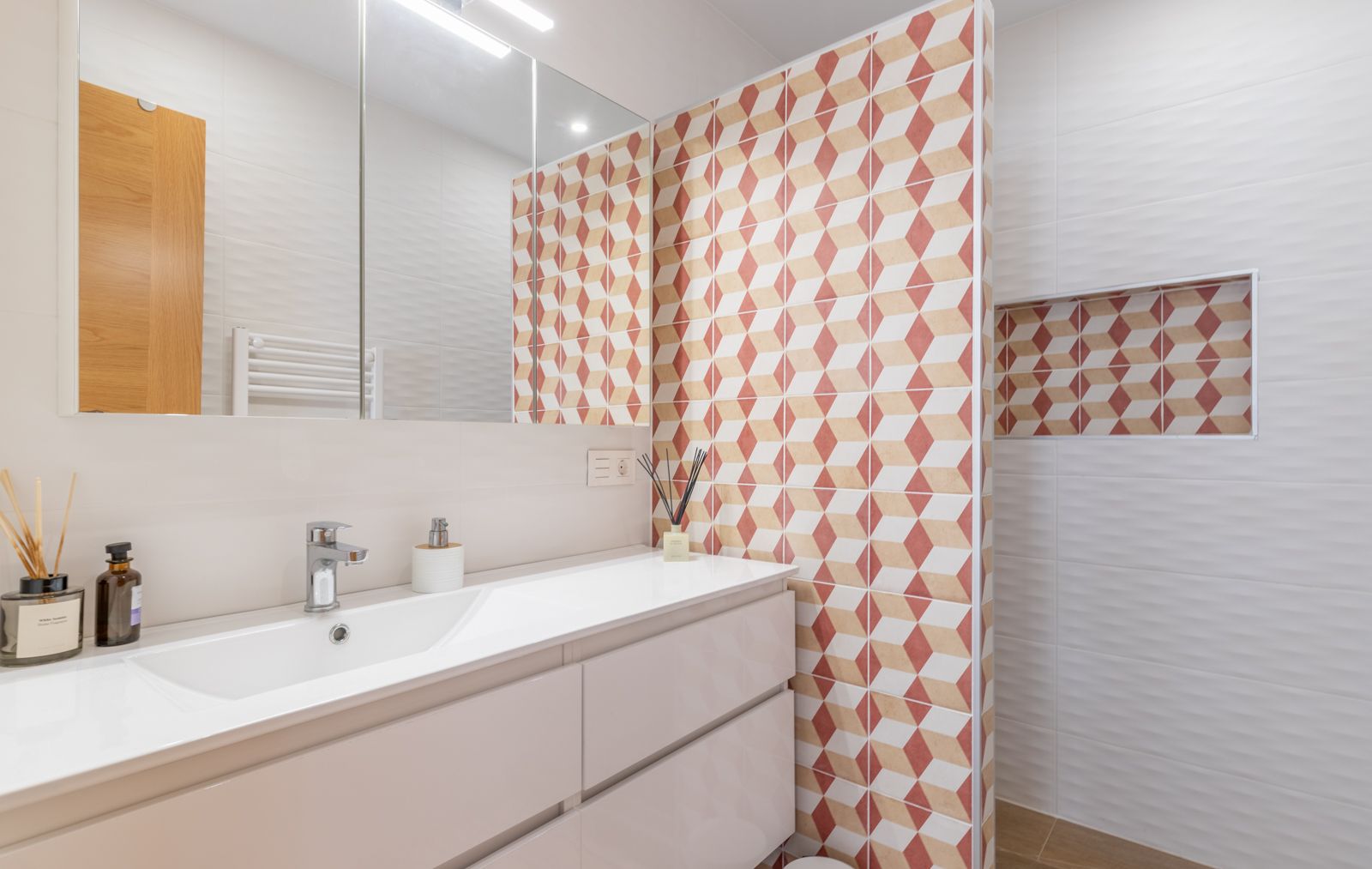 Modernes Badezimmer mit weißem Waschtisch, Spiegelschrank und Akzentwand mit geometrischen Fliesenmustern sowie einer integrierten Wandnische.
