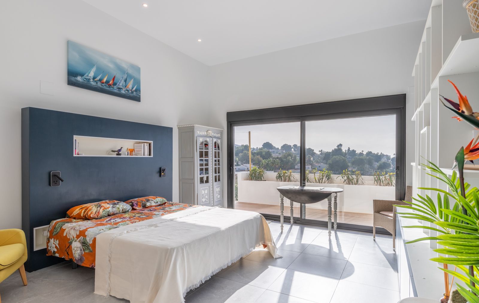 Modernes Schlafzimmer mit dunkelblauer Akzentwand, integrierter Nische und direktem Zugang zur Terrasse durch große Glasschiebetüren.