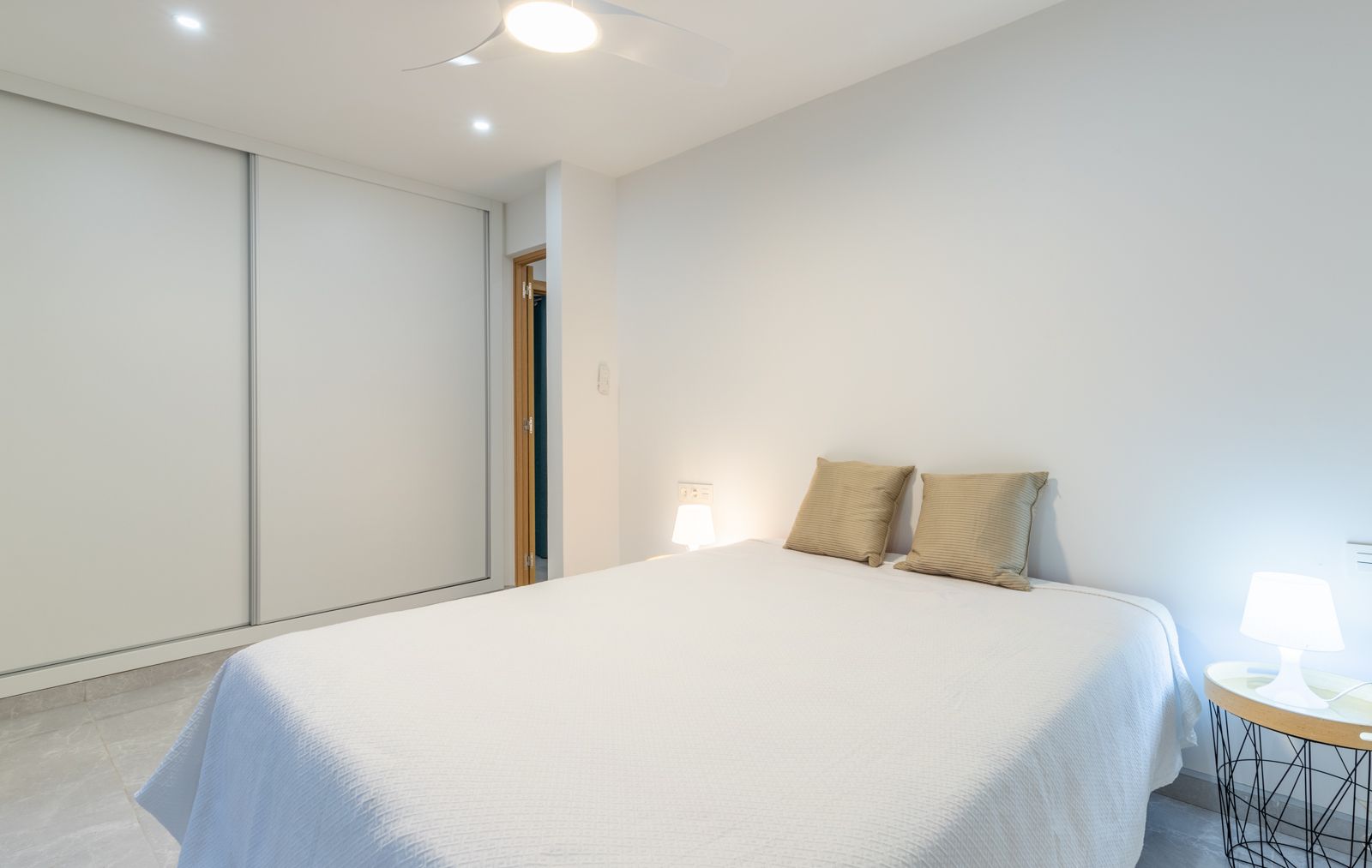 Modernes Schlafzimmer mit großem weißem Schiebetürenschrank, grauen Feinsteinzeugfliesen und integriertem Deckenventilator in minimalistischem Design.