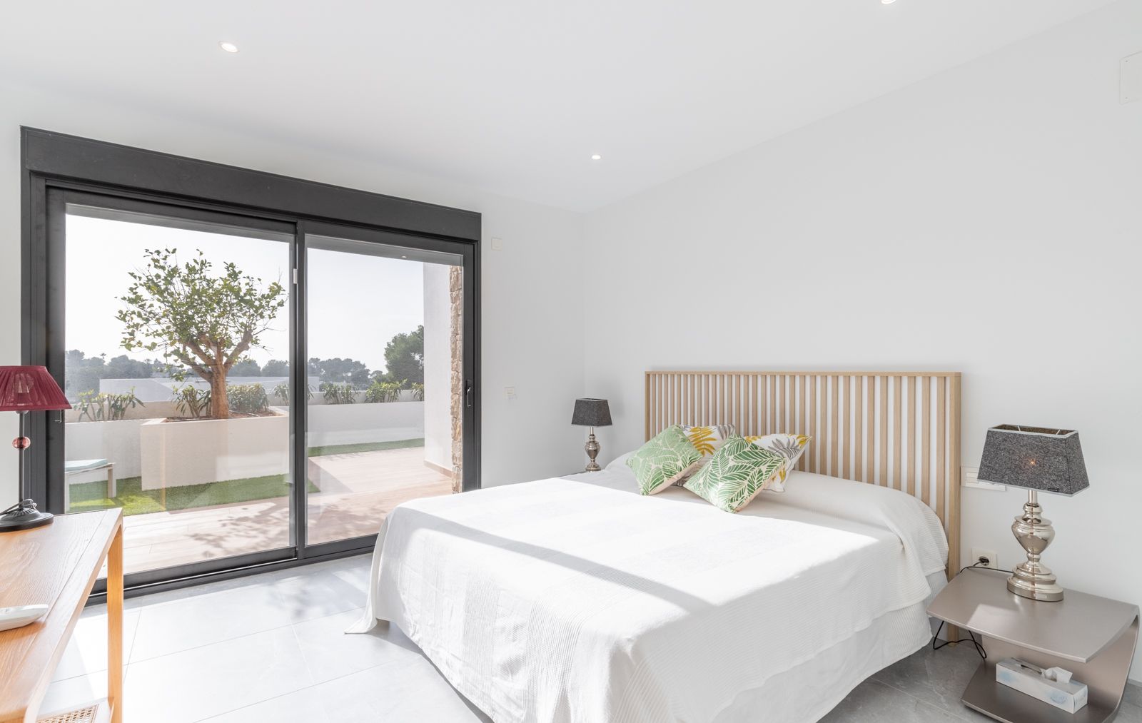 Modernes Schlafzimmer mit Kopfteil aus Holzlamellen, großen Glasschiebetüren zur privaten Terrasse und hellen Feinsteinzeugböden.