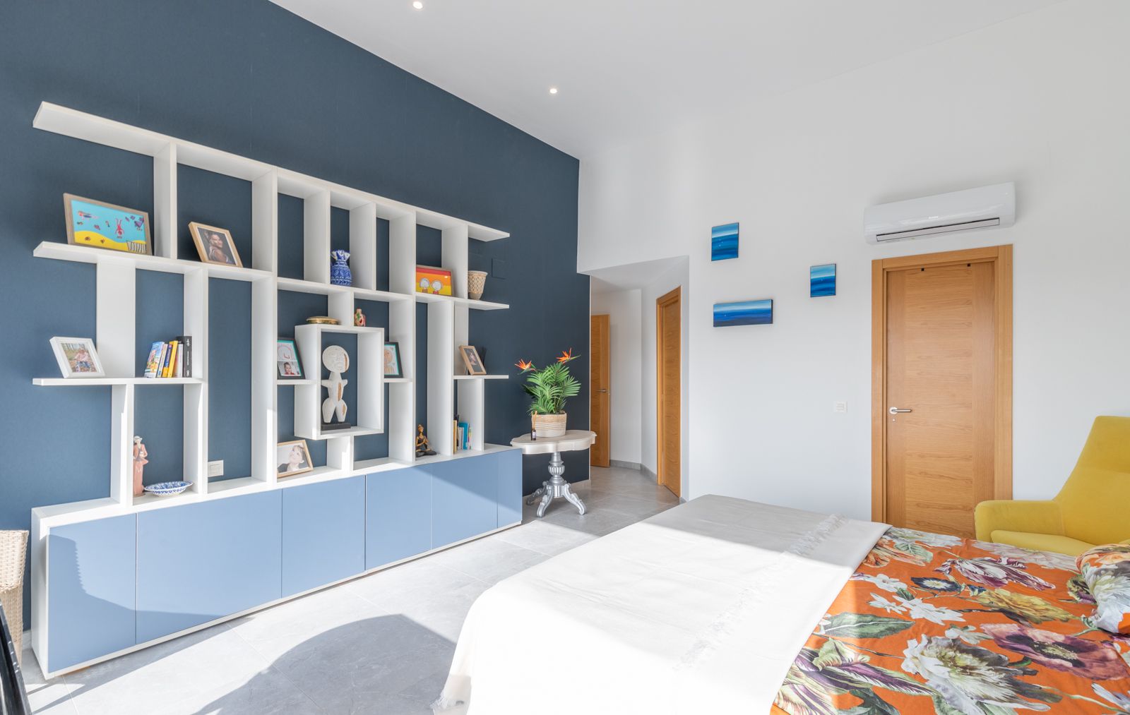 Modernes Schlafzimmer mit weißem geometrischem Regal vor dunkelblauer Akzentwand, integrierten Schränken und hellem Feinsteinzeugboden.