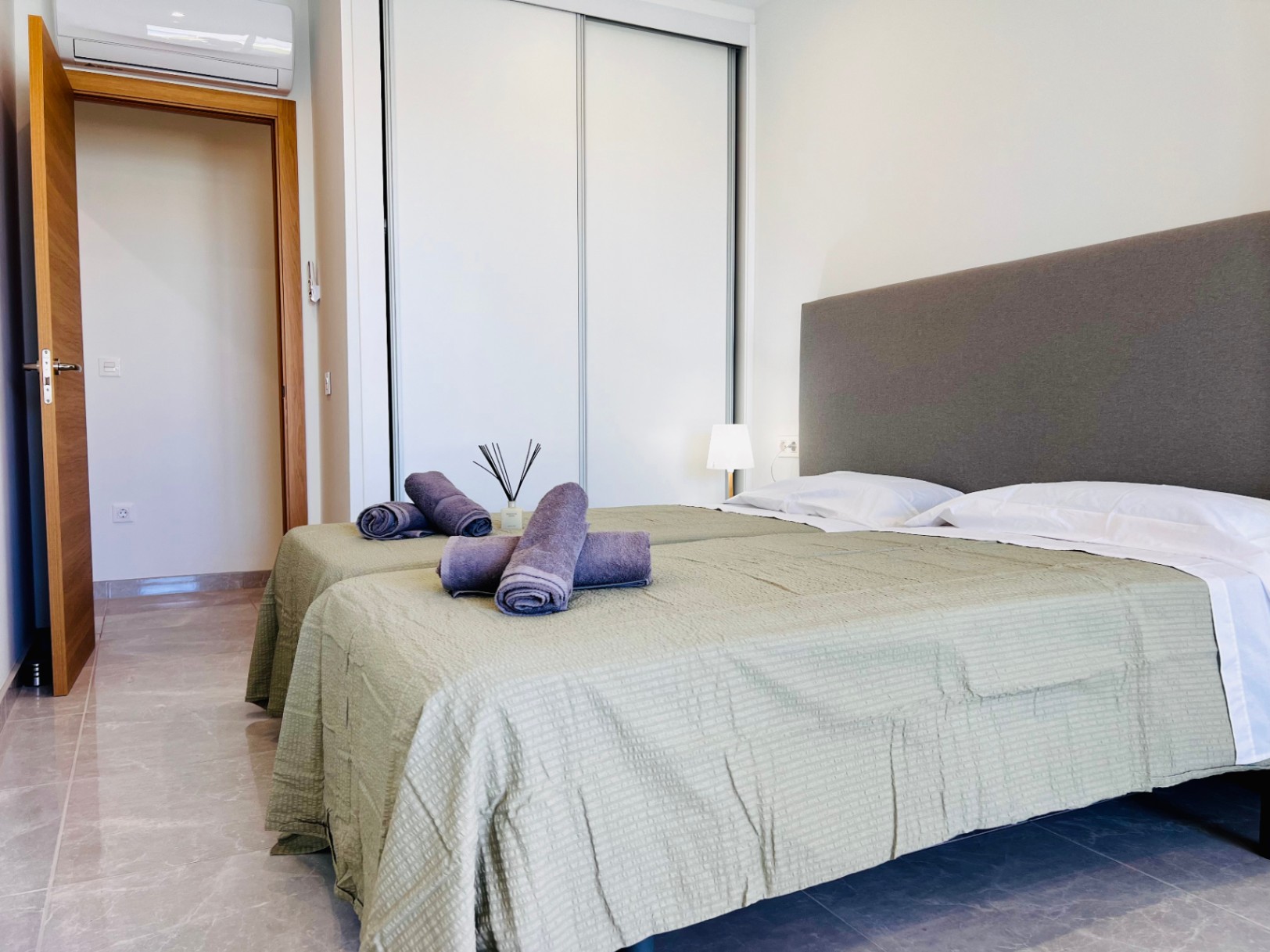 Modernes Schlafzimmer mit weißen Einbauschränken, Feinsteinzeugböden und Split-Klimaanlage. Innentüren aus Naturholz ergänzen das zeitgemäße, minimalistische Design.