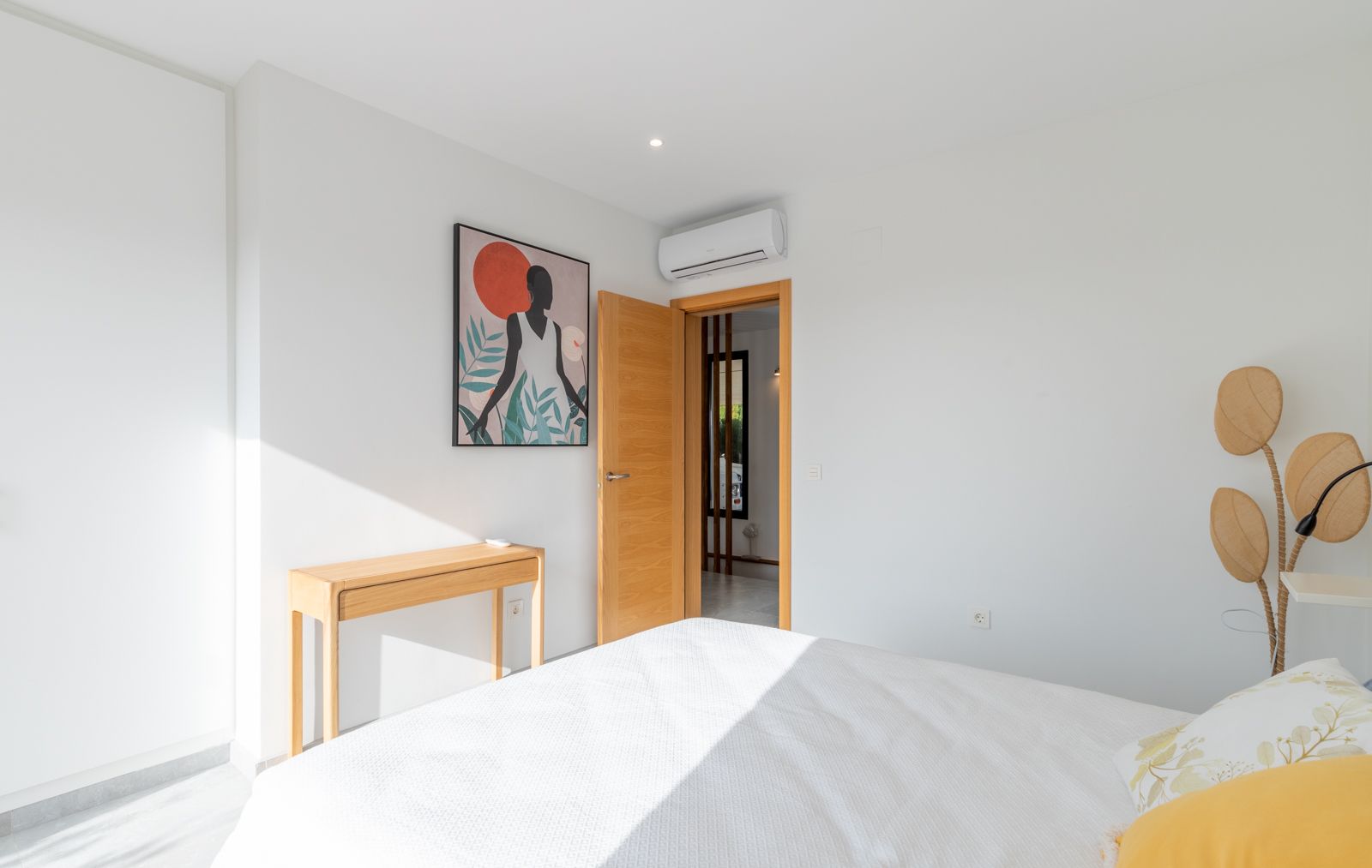 Modernes Schlafzimmer mit weißen Wänden, Konsoltisch aus Naturholz und Split-Klimaanlage. Es besticht durch helle Holzschreinerei und zeitgenössisches Dekor.