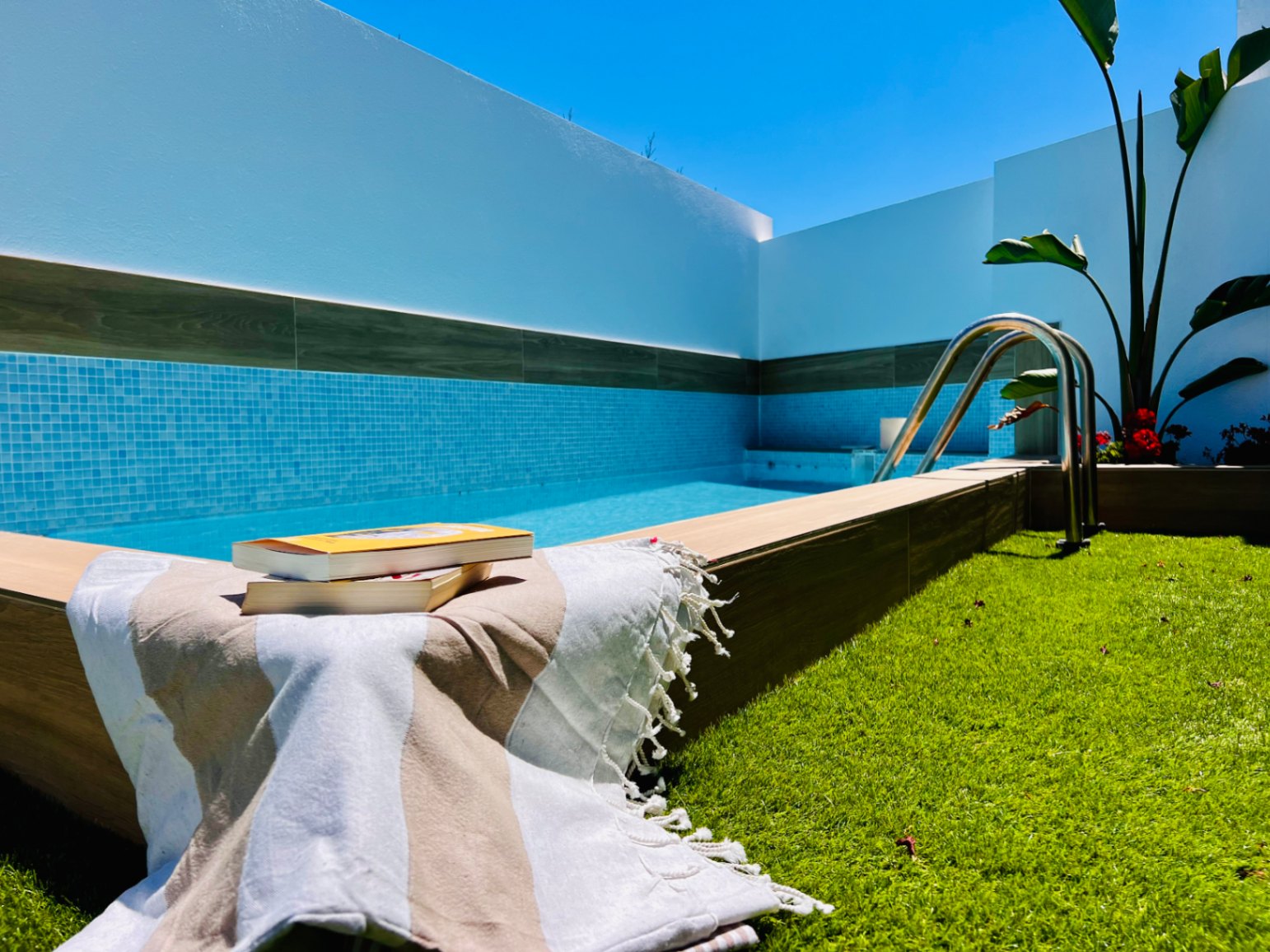 Privater Jacuzzi mit blauen Mosaikfliesen, Holzoptik-Einfassung und Kunstrasenbereich, umgeben von weißen Mauern und mediterraner Bepflanzung.