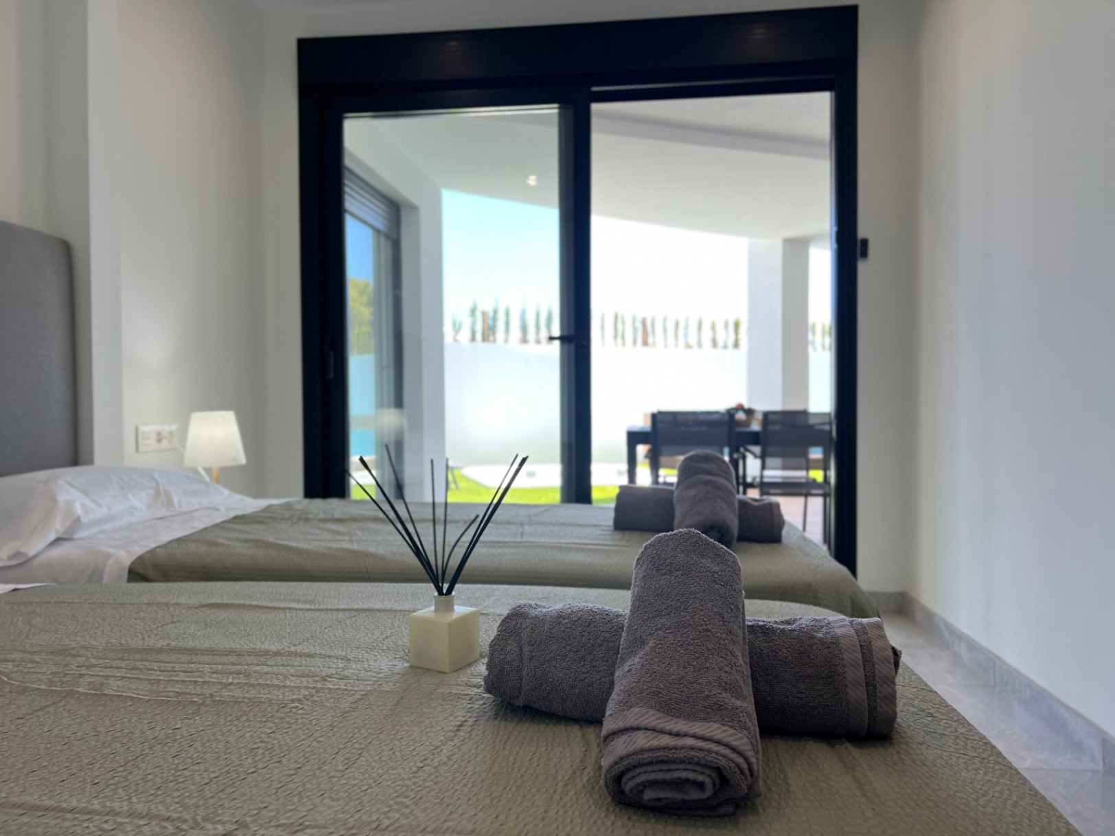 Schlafzimmer mit zwei Einzelbetten und direktem Zugang zur Terrasse durch große, schwarz gerahmte Glasschiebetüren in hellem, modernem Design.