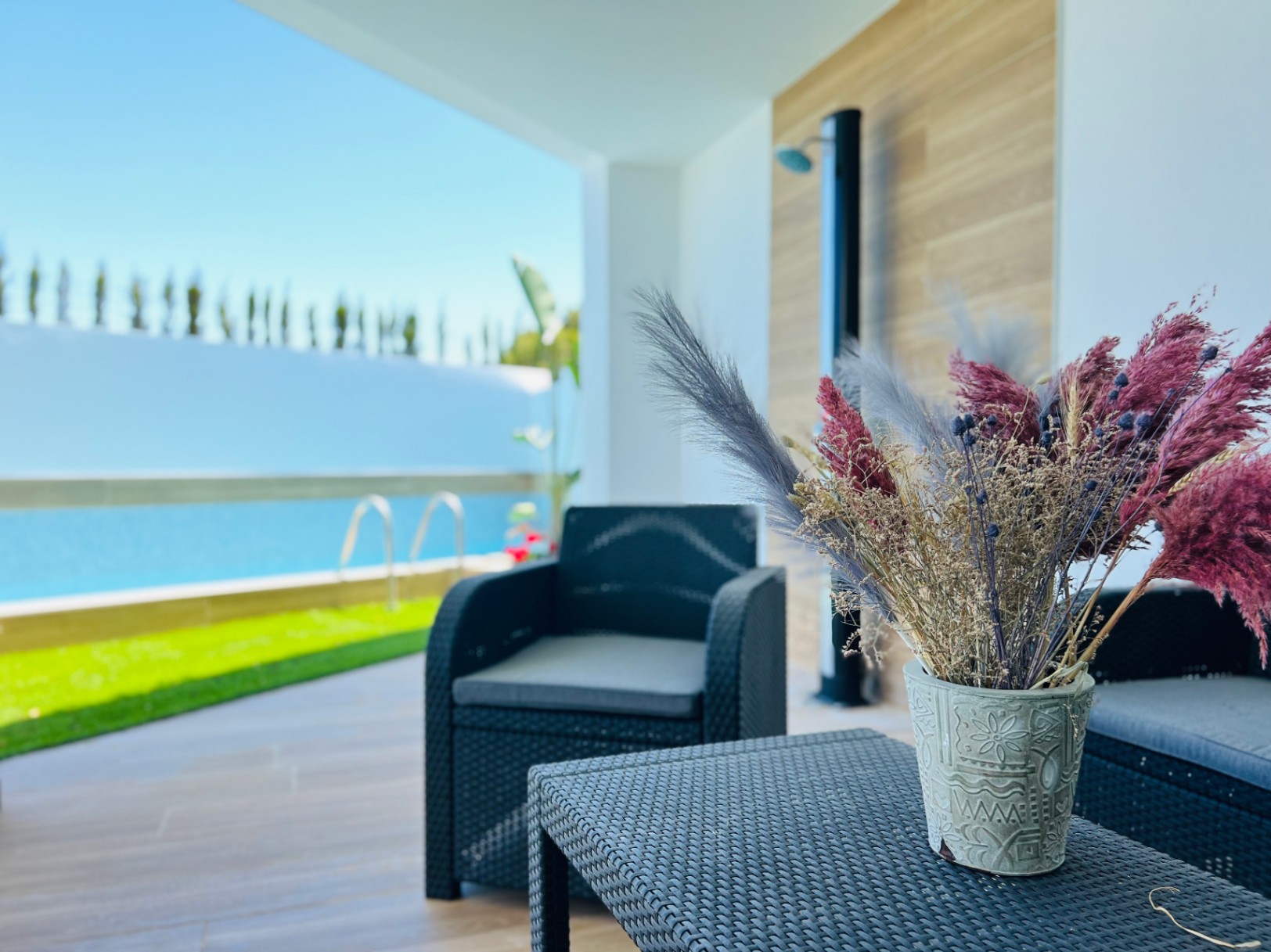 Überdachte Terrasse mit dunklen Rattanmöbeln und Blick auf den privaten Poolbereich sowie die gepflegte Gartenanlage.