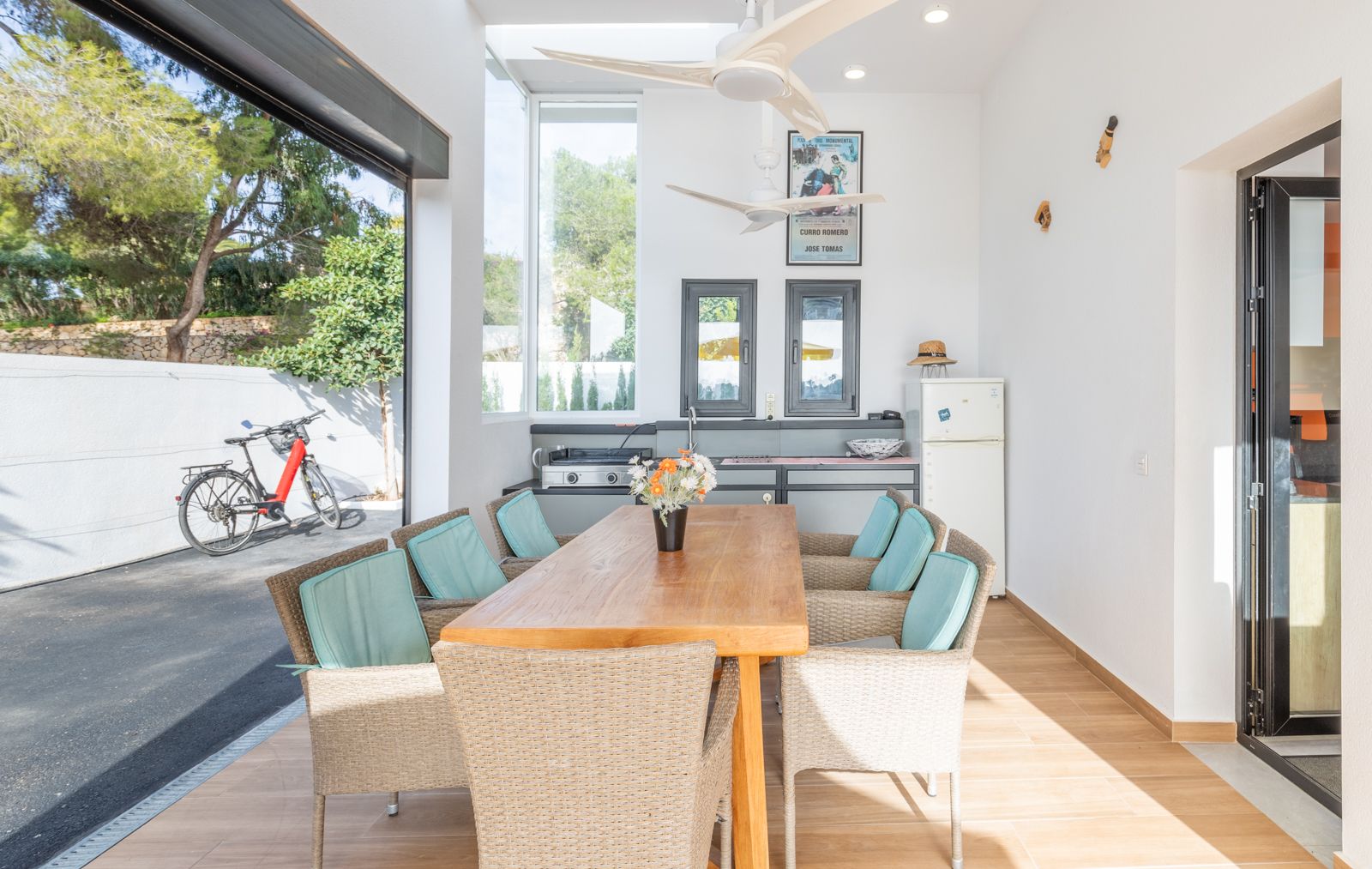 Überdachter Außenessbereich mit Sommerküche, massivem Holztisch, Korbstühlen und Deckenventilatoren, mit direktem Zugang zum gepflasterten Hof.