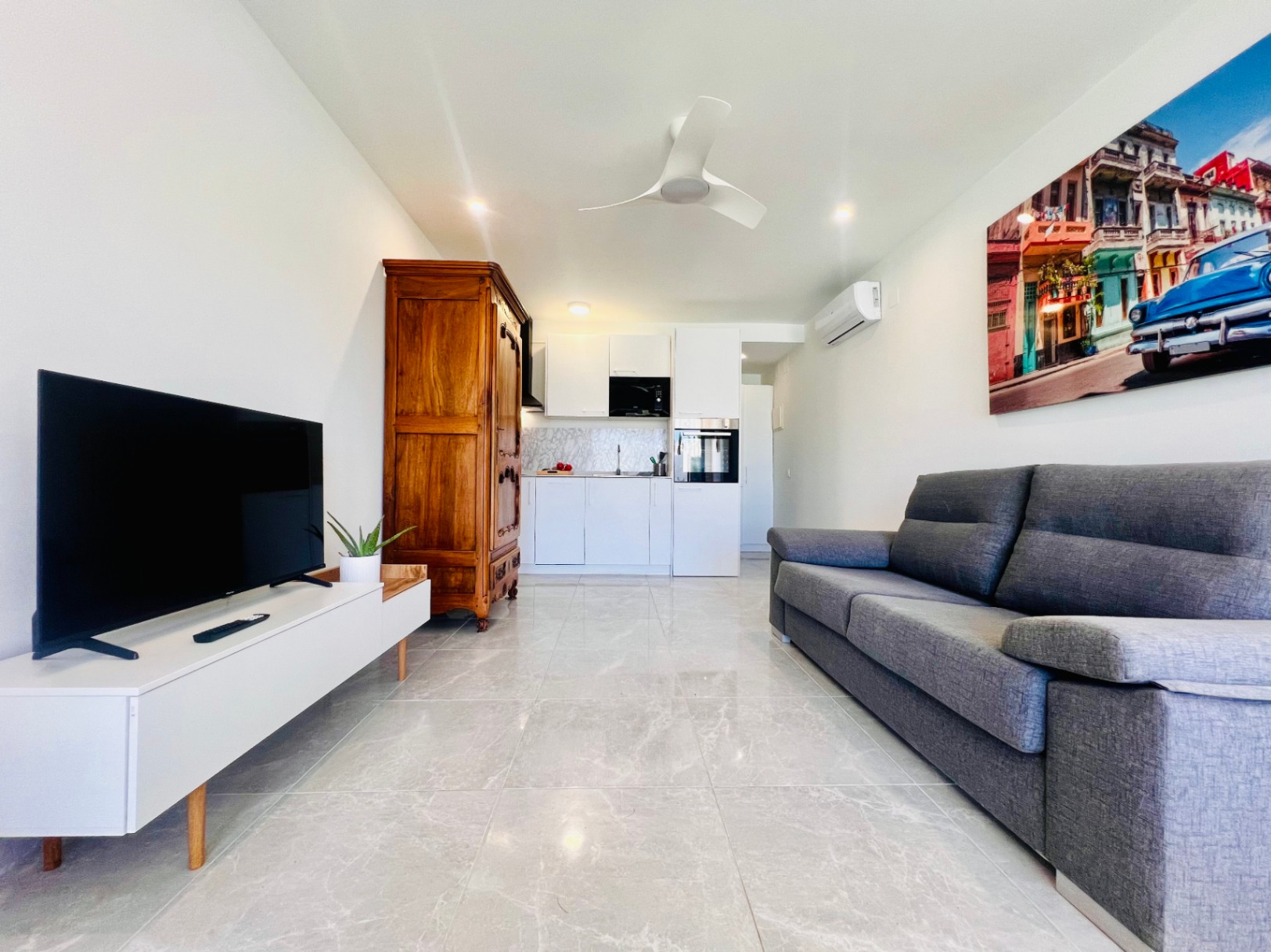 Wohnbereich eines Gästeapartments mit Marmoreffekt-Fliesen, moderner Küchenzeile, grauem Sofa und einem markanten klassischen Holzschrank als Kontrast.