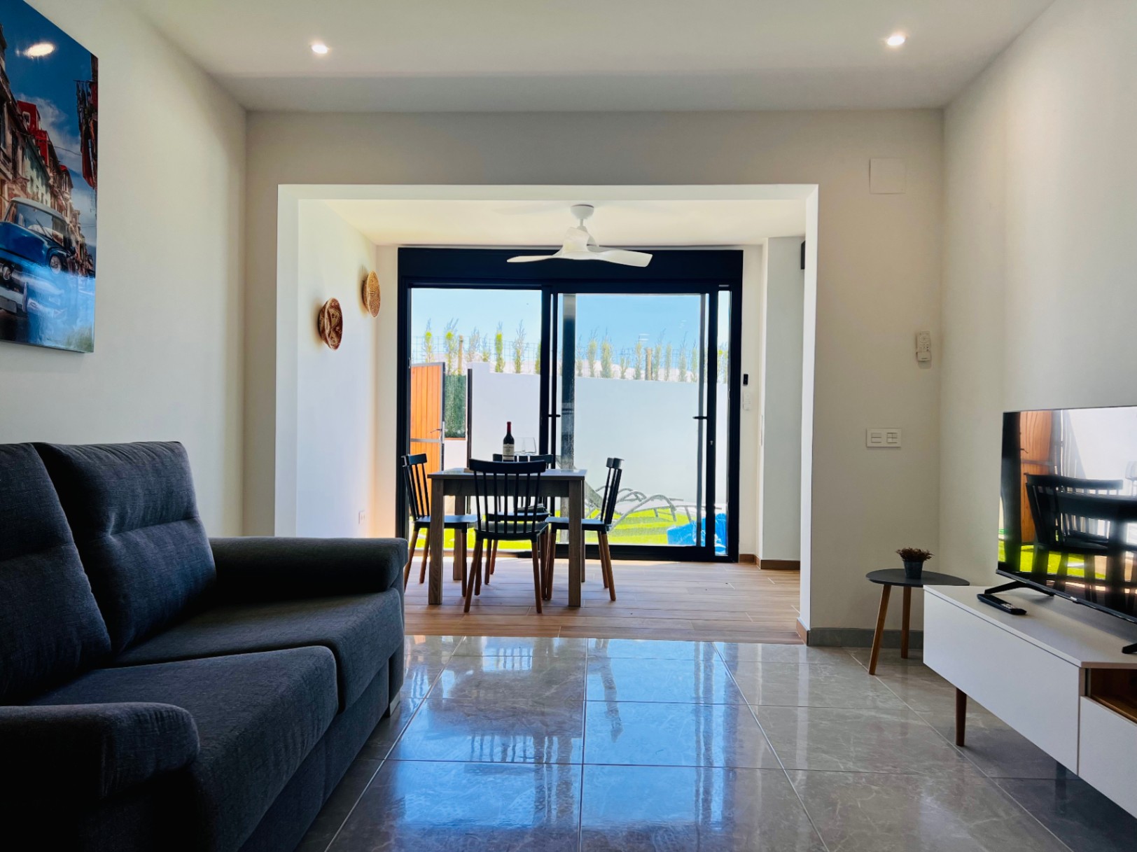 Zeitgenössisches Wohnzimmer mit polierten Fliesenböden, grauem Sofa und integriertem Essbereich mit Deckenventilator und Glasschiebetüren zum Außenbereich.