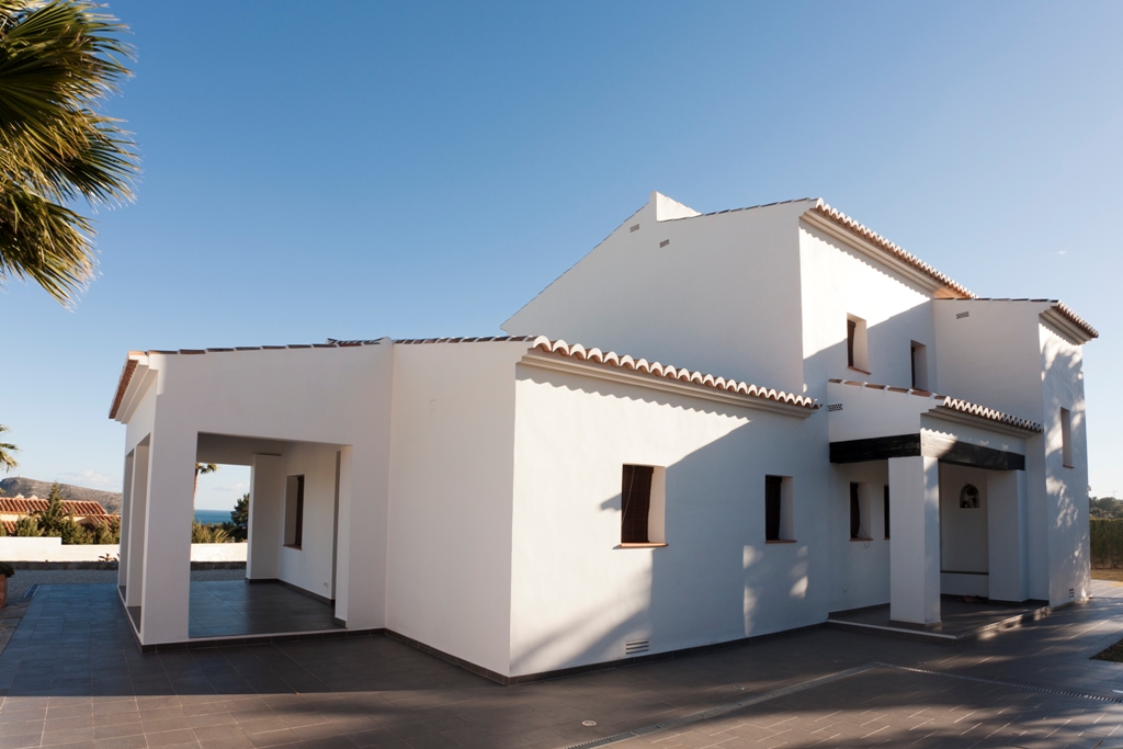 Außenansicht der mediterranen Villa mit weißen Fassaden, Terrakotta-Dachziegeln und großzügigen gefliesten Terrassen, die zu einer überdachten Veranda führen.