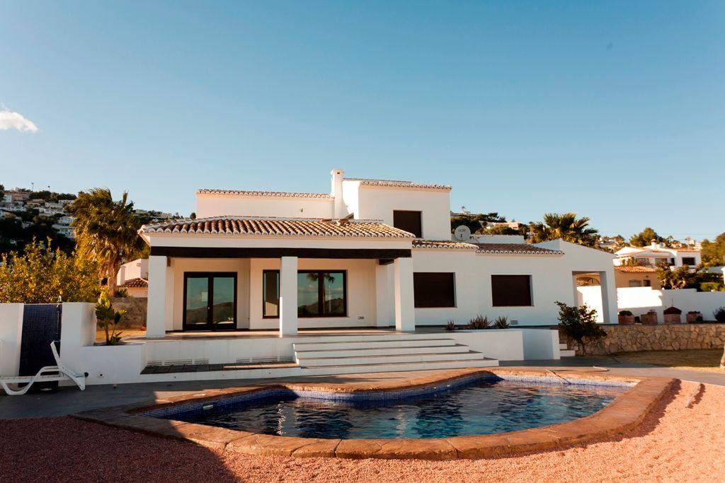 Außenansicht der Villa mit nierenförmigem Pool, überdachter Veranda mit dunklen Holzbalken und weißer Fassade im mediterranen Stil.