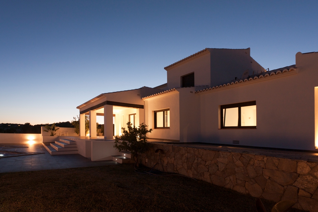 Außenfassade der Villa in der Abenddämmerung mit warmer Beleuchtung, Natursteinmauern und Terrassen, die direkt zum Poolbereich führen.