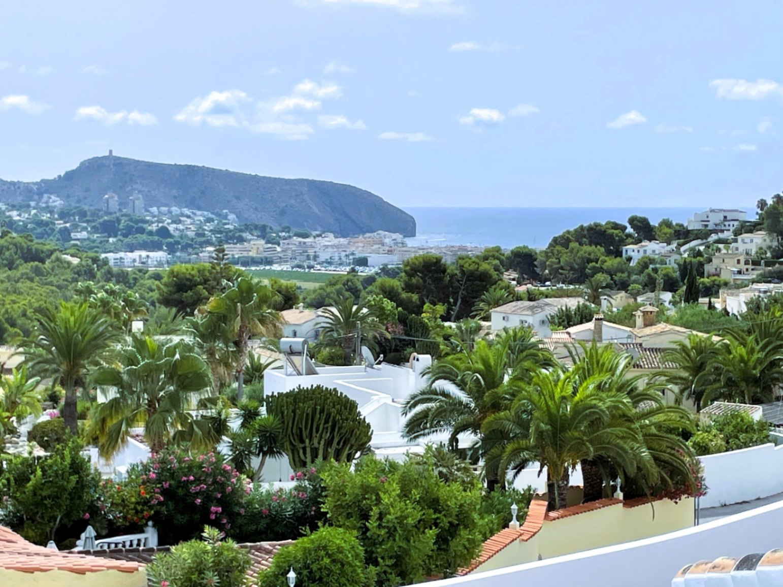 Erhöhter Panoramablick auf die Küste von Moraira, das Mittelmeer und das Cap d'Or, eingebettet in eine üppige mediterrane Gartenlandschaft.