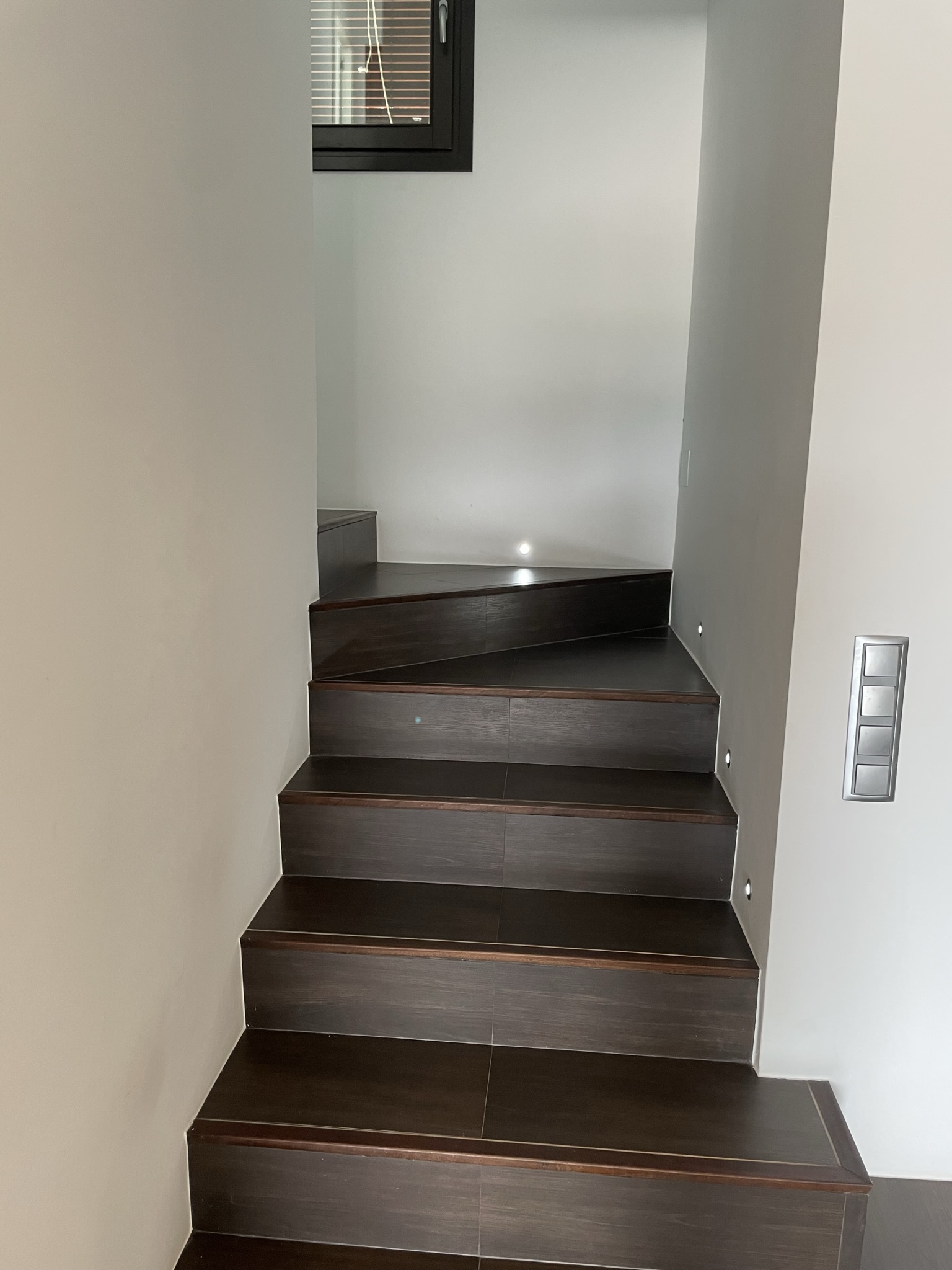 Innentreppe mit dunklen Stufen in Holzoptik, integrierter LED-Wandbeleuchtung und glatten weißen Wänden in modernem Design.