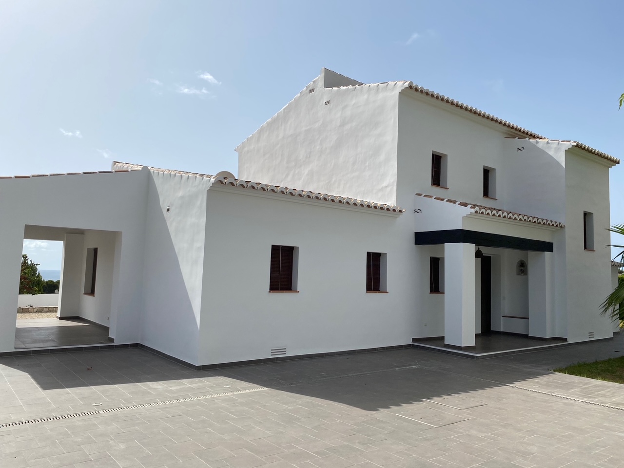 Mediterrane Fassade mit weißen Wänden, Terrakotta-Ziegeldächern und einem weitläufigen, grau gefliesten Außenbereich mit Entwässerungsrinnen.