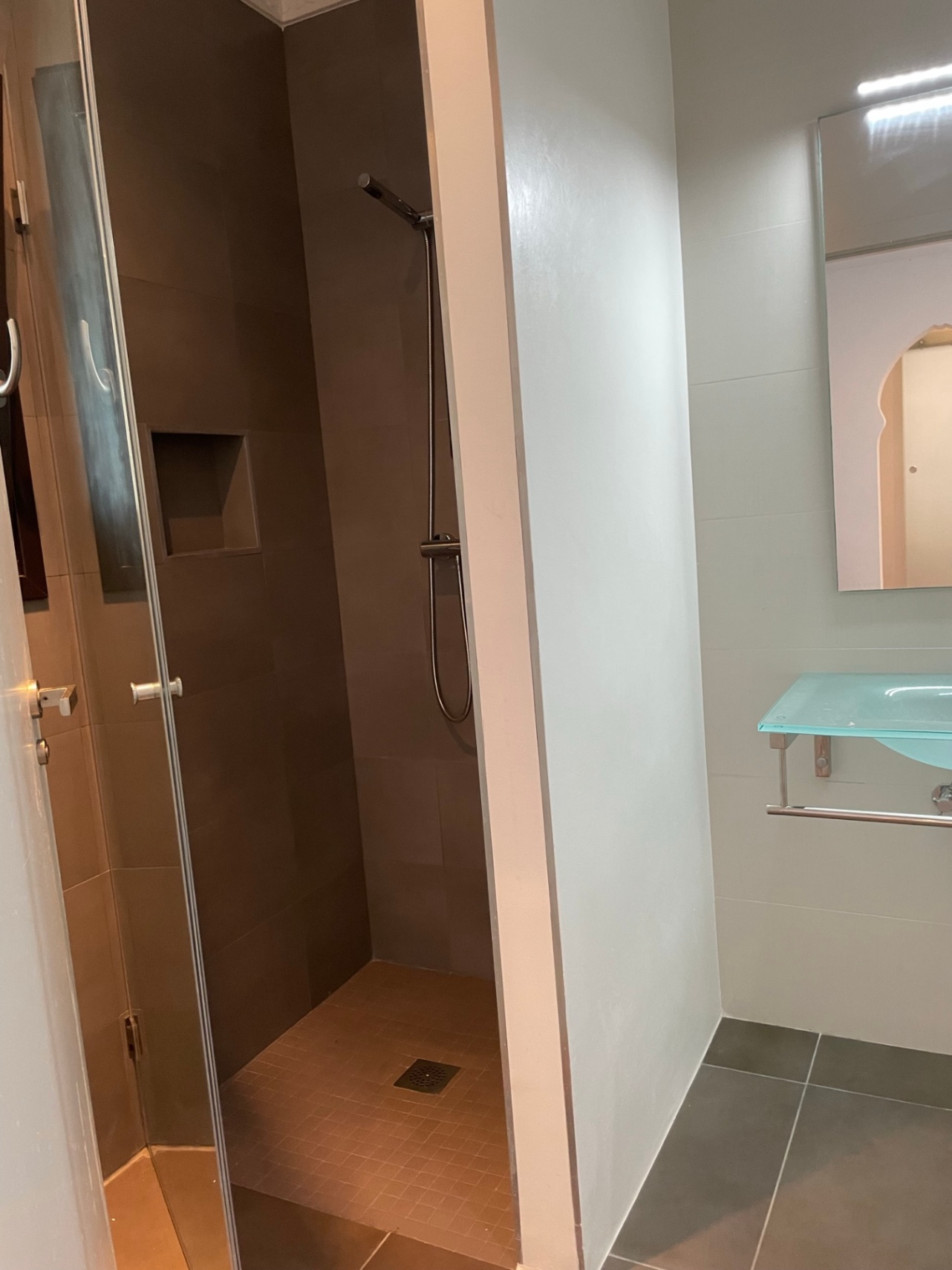 Modernes Badezimmer mit begehbarer Dusche in Erdtönen, integrierter Wandnische und einem eleganten Glaswaschbecken.