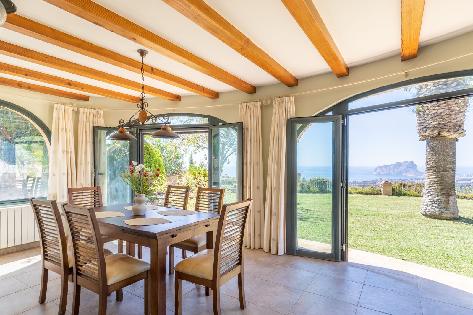 Heller Speisesaal mit Holzbalken und Blick auf den Garten und das Mittelmeer.
