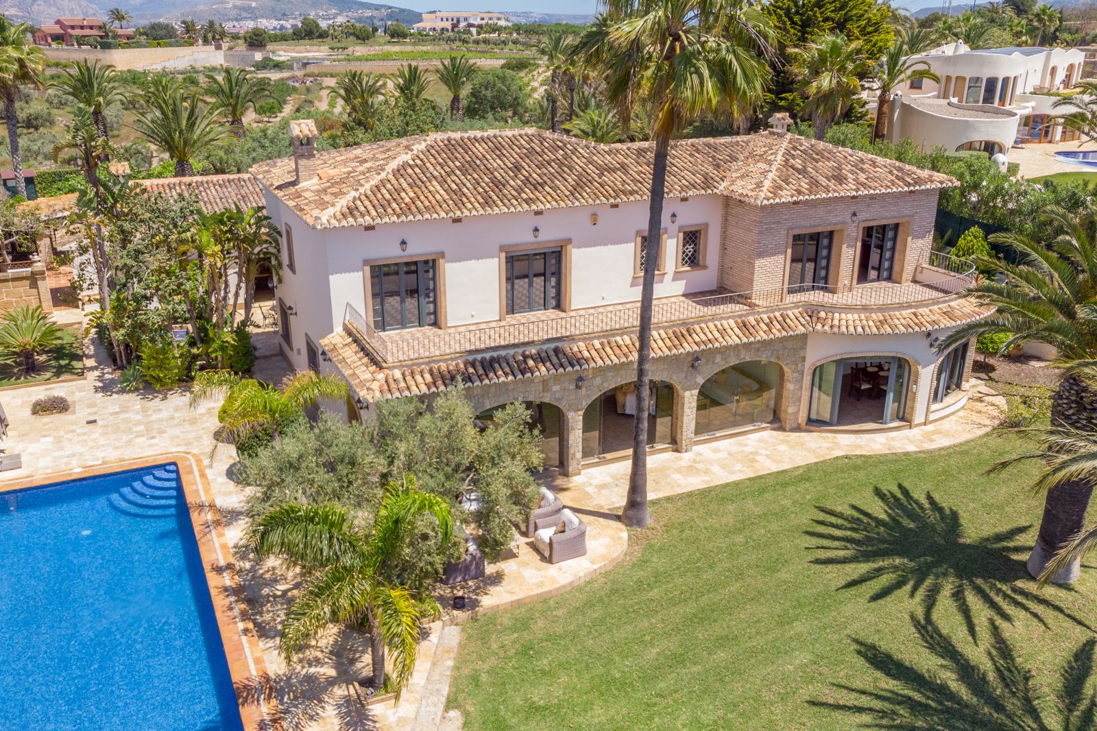 Luftaufnahme der Villa mit Pool, Garten und überdachter Terrasse mit Steinbögen.