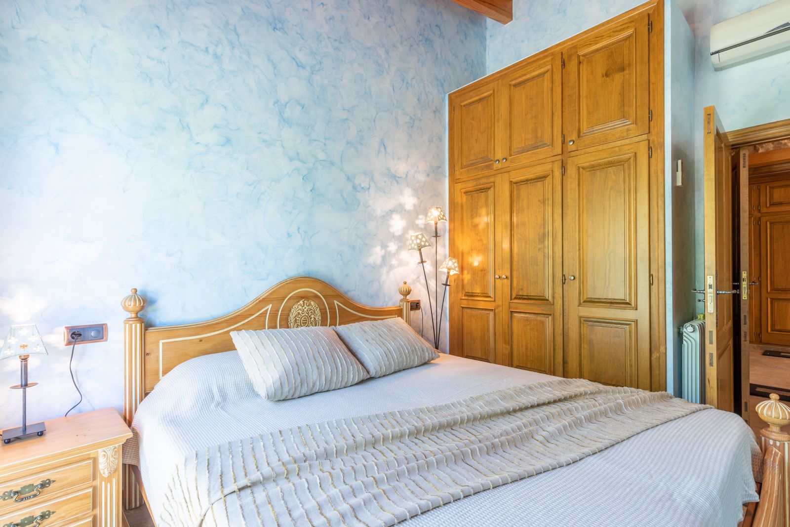 Schlafzimmer mit strukturierter blauer Wand, hellem Holzbettrahmen und eingebautem Holzschrank.