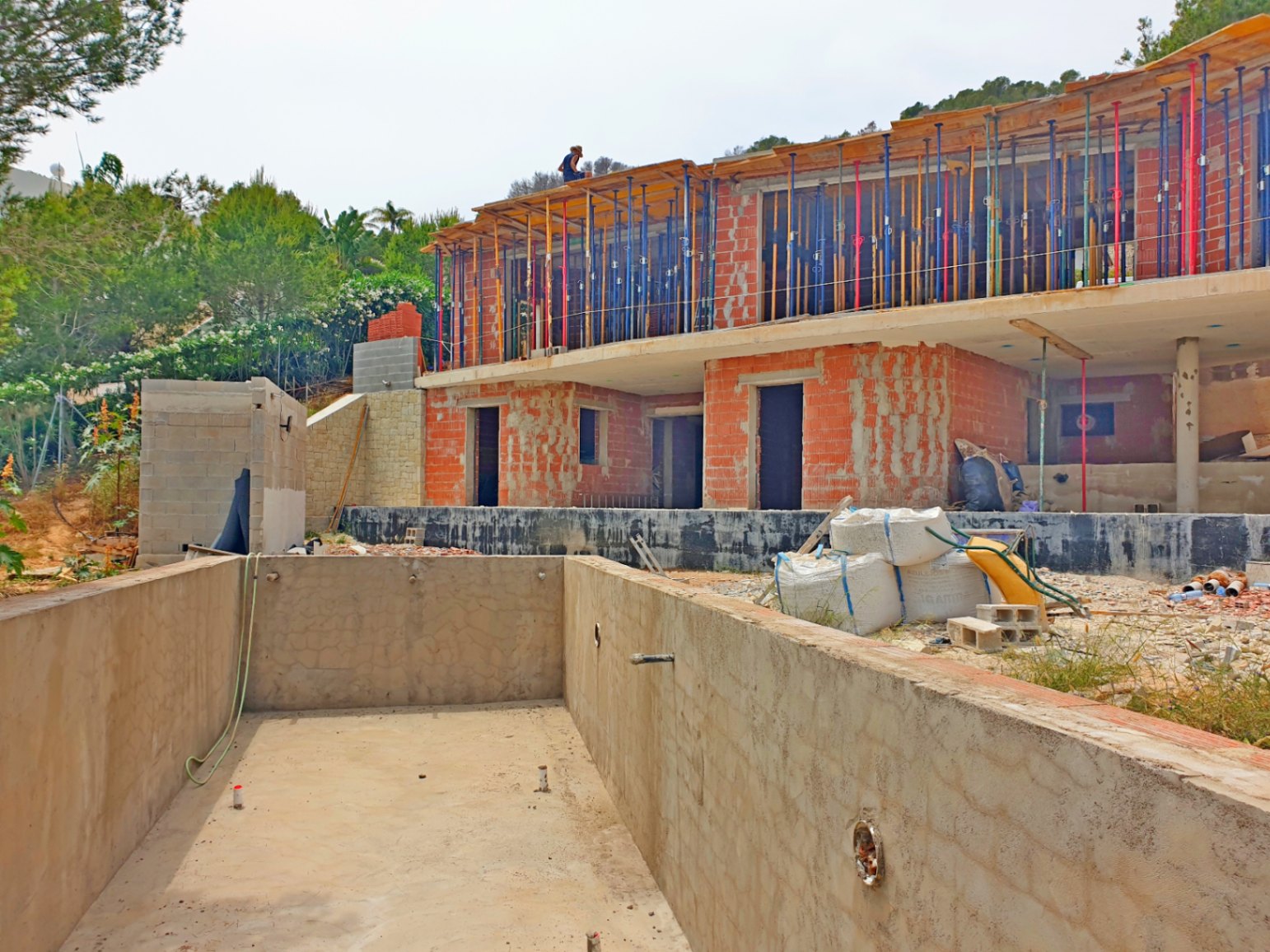 Aktueller Baustatus mit der zweistöckigen Backsteinstruktur, Metallstützen und dem Betonbecken des Pools im Vordergrund.