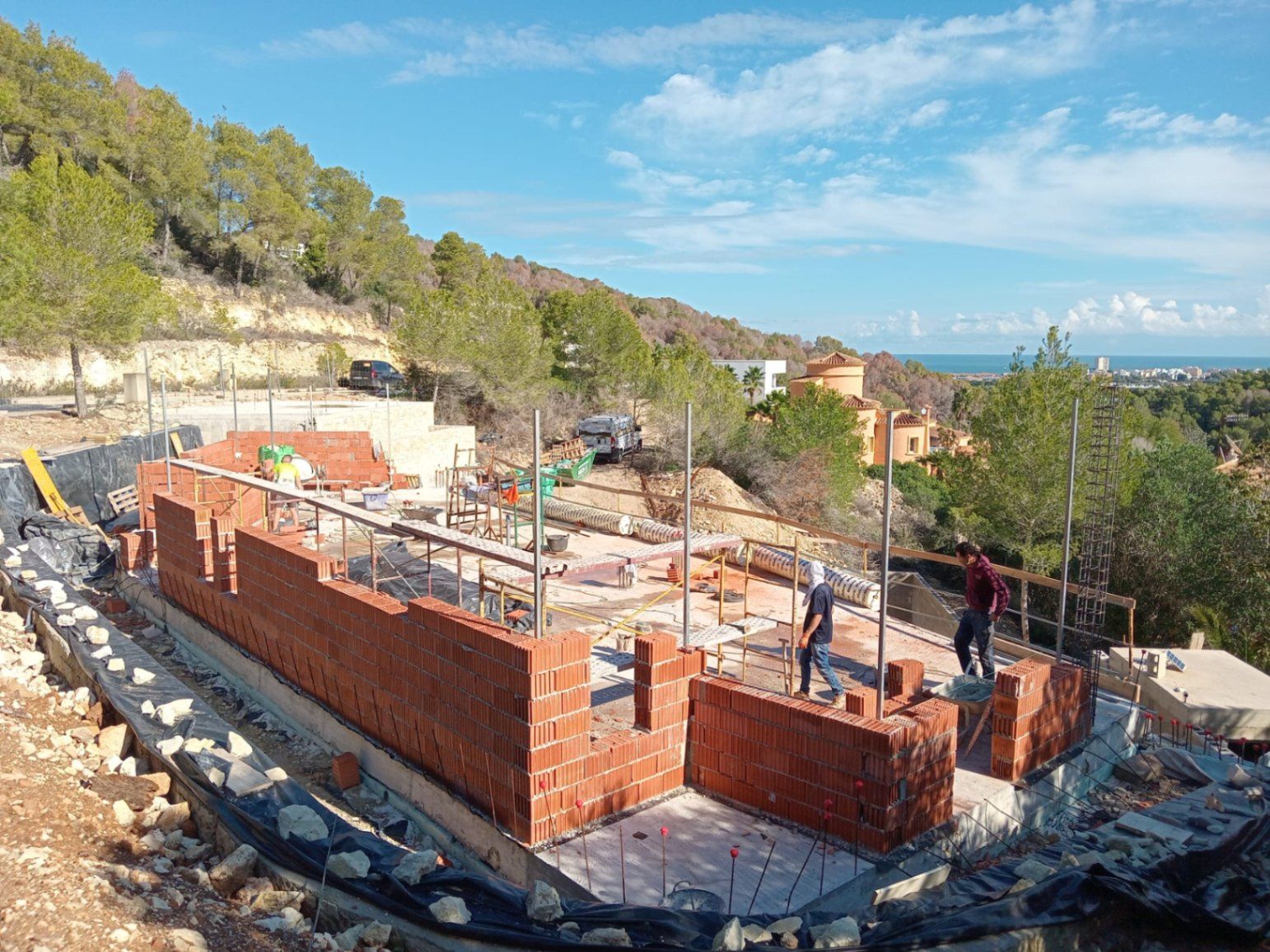 Erste Bauphase der Villa in Jávea mit Mauerwerksarbeiten auf dem Fundament und weitem Blick über die Hügel bis hin zum Mittelmeer.